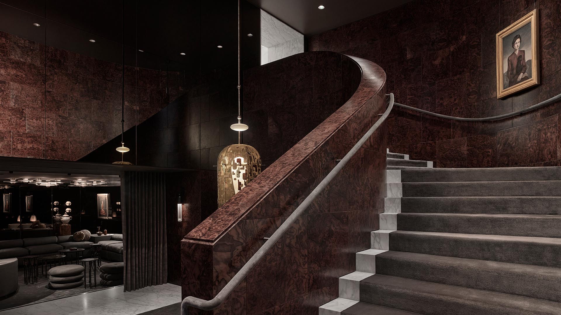 Curved staircase with dark textured walls, modern pendant lights, and framed artwork above the landing in dim interior space