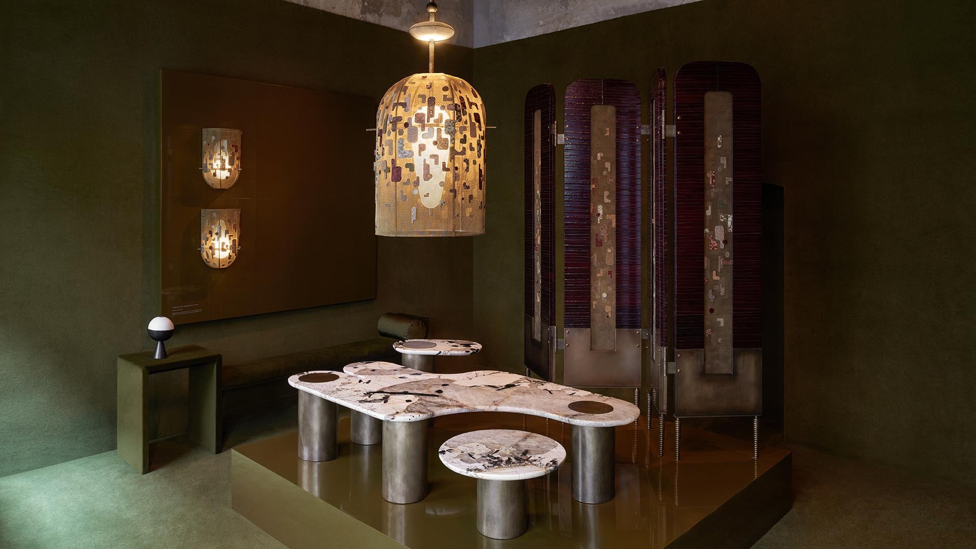 Contemporary room with sculptural pendant light, abstract stone tables with cylindrical bases, and textured folding screens on green walls
