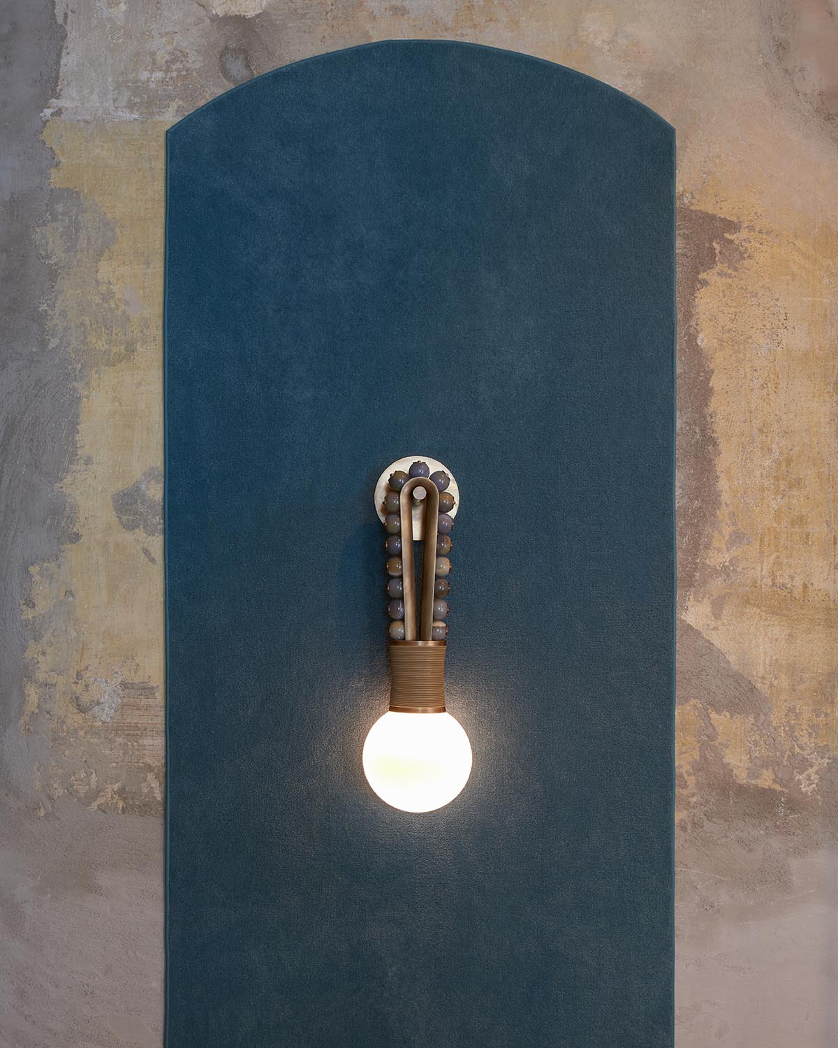 Wall-mounted vintage style light bulb fixture on dark blue textured panel against distressed plaster wall