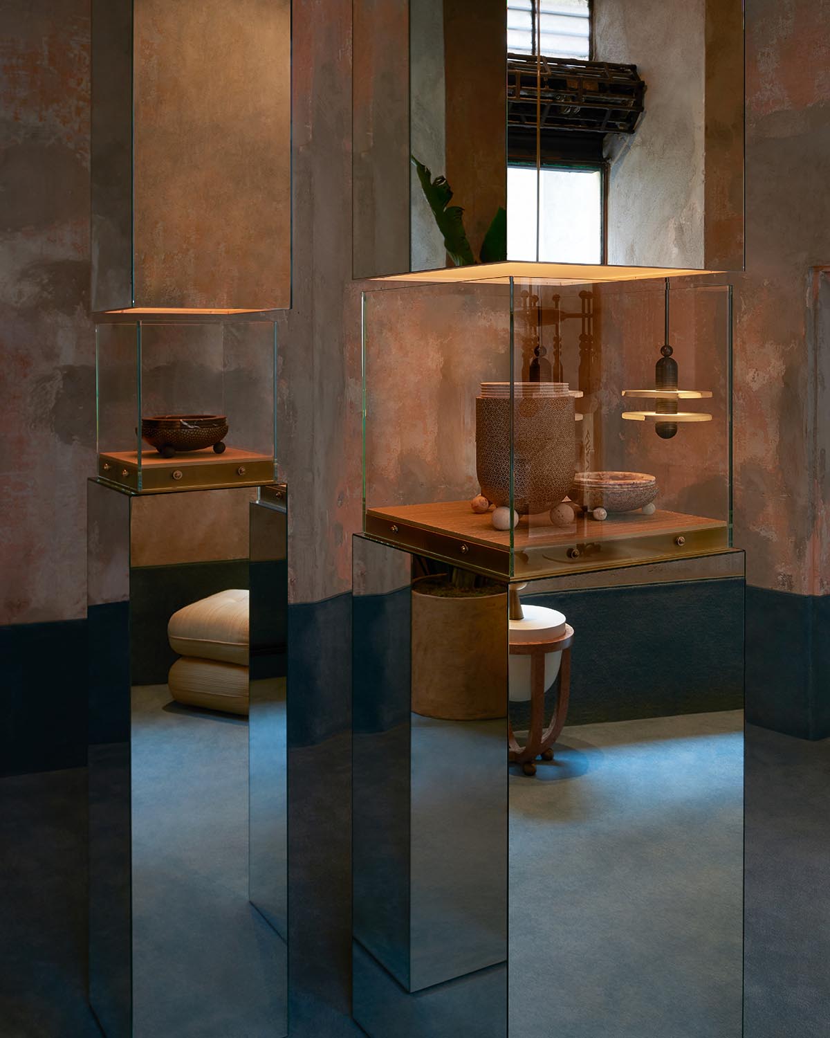 Exhibition space with glass display cases containing pottery and small art objects on mirrored pedestals in a dimly lit room