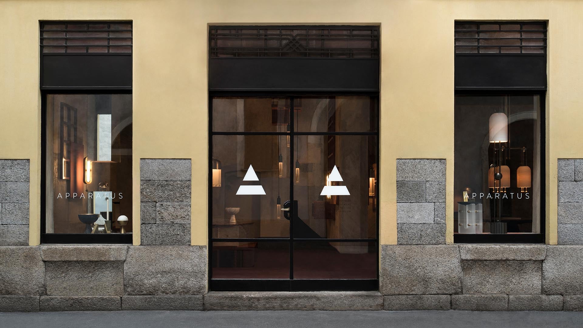 Exterior view of a minimal storefront with large glass windows and doors featuring geometric white logo symbols on a stone base wall