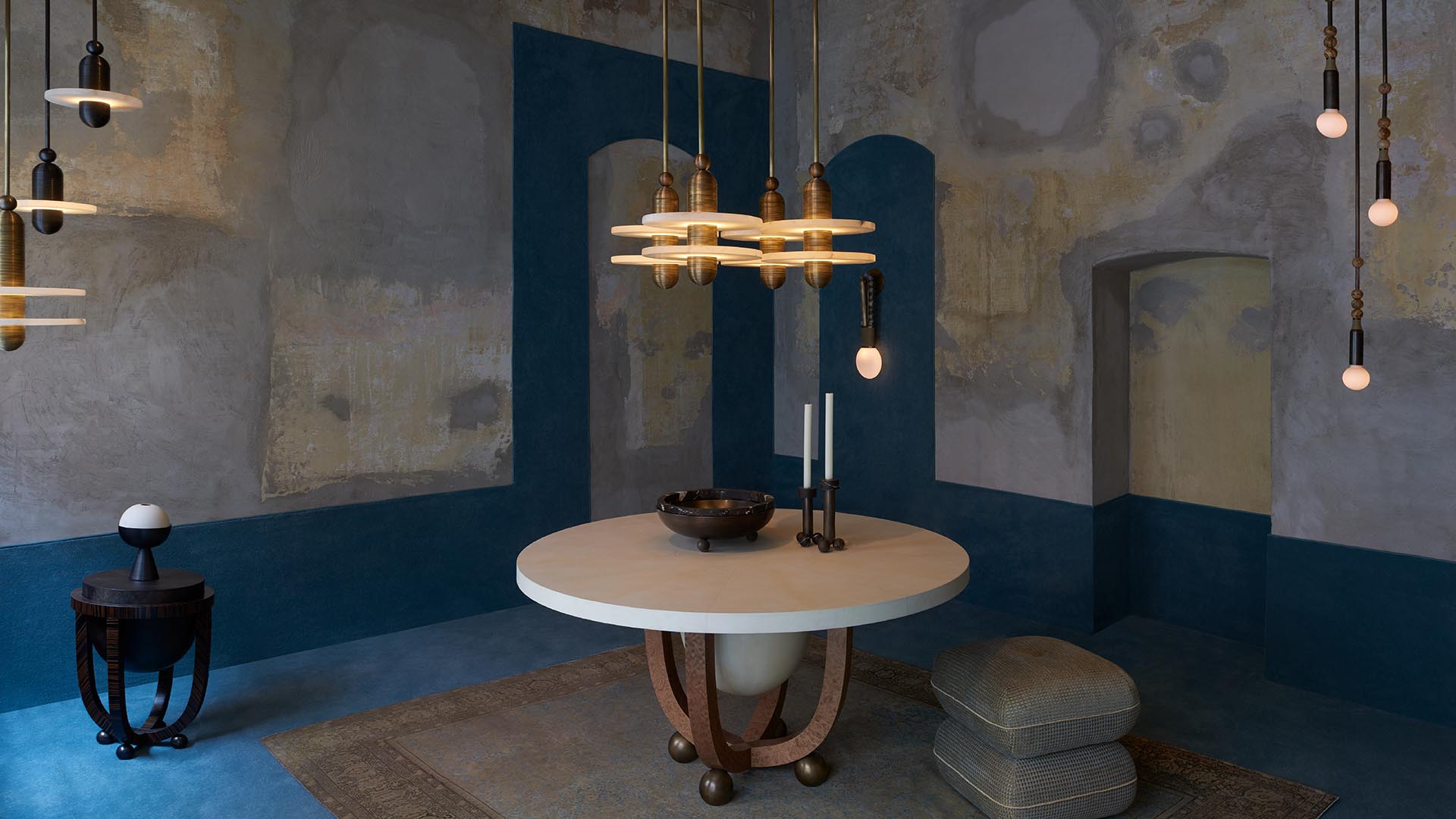 Minimalist room with a round white table, modern pendant lights, textured walls, and a small round side table with a lamp