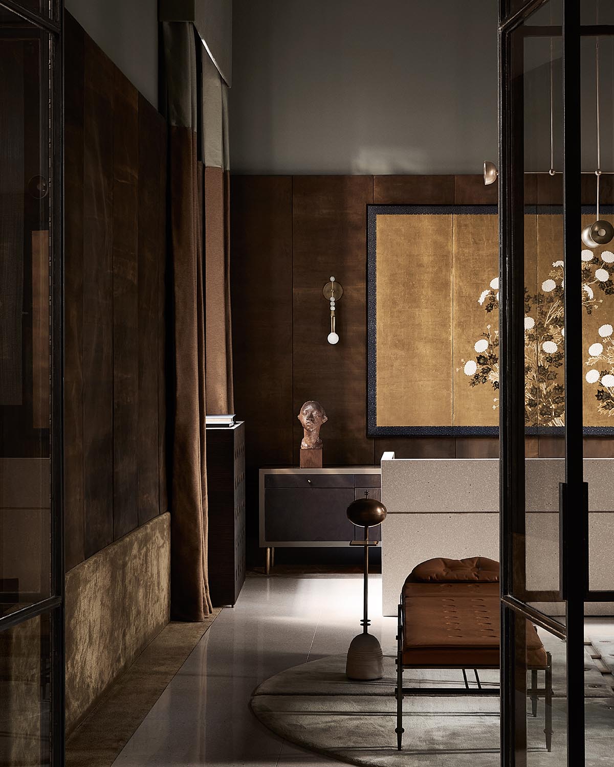 Dimly lit interior with brown textured walls, a sculpted bust on a dark sideboard, and a large gold and black framed artwork.