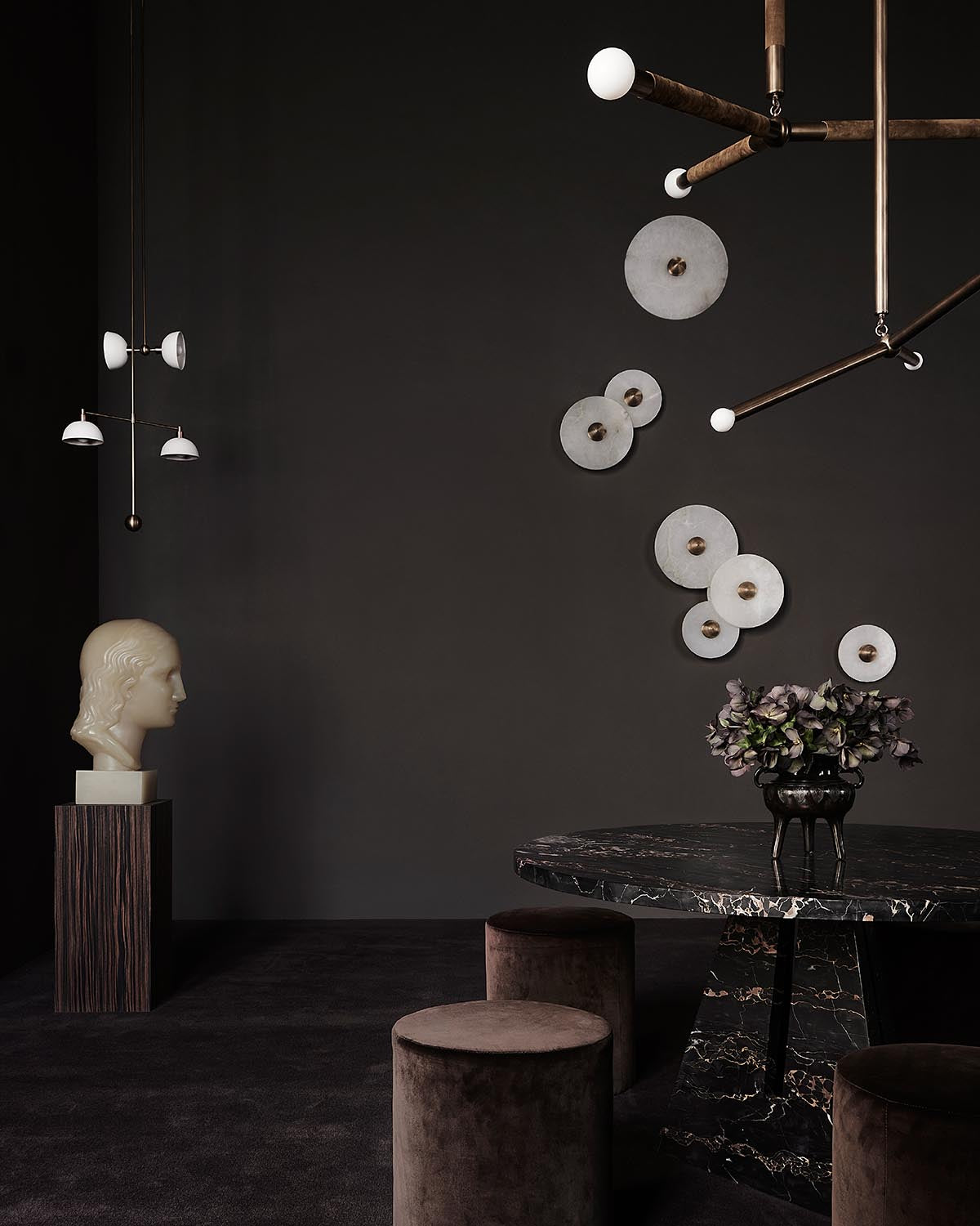 Dark minimalist room with marble round table, velvet stools, abstract wall decor, and sculpted head bust on pedestal