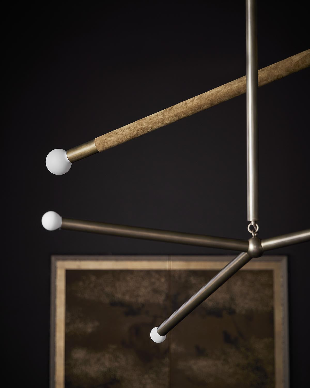 Close-up of modern chandelier with brass arms and white spherical bulbs against a dark wall with abstract artwork