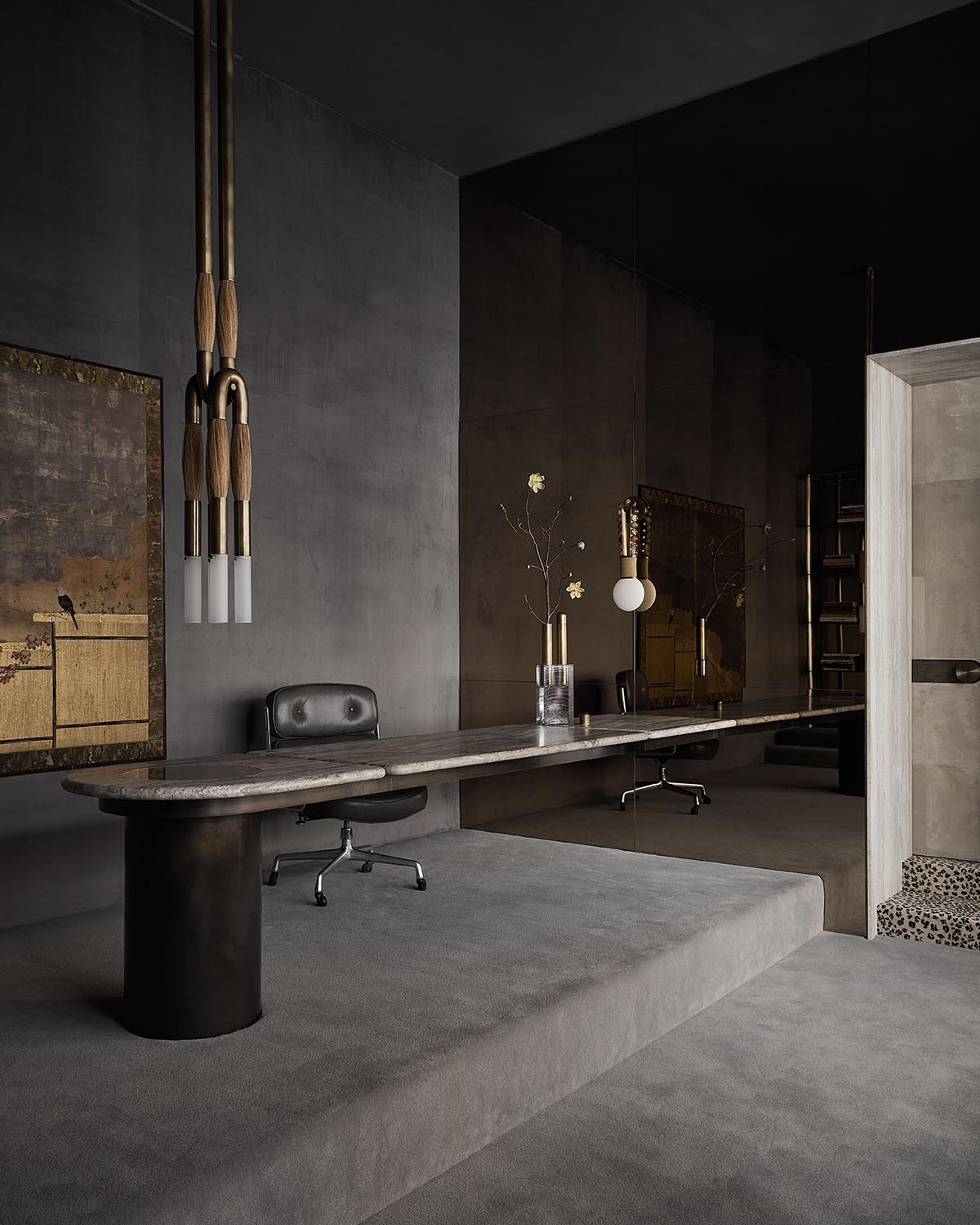 Minimalist interior with long stone table, black swivel chairs, pendant lights, and textured dark walls with framed art