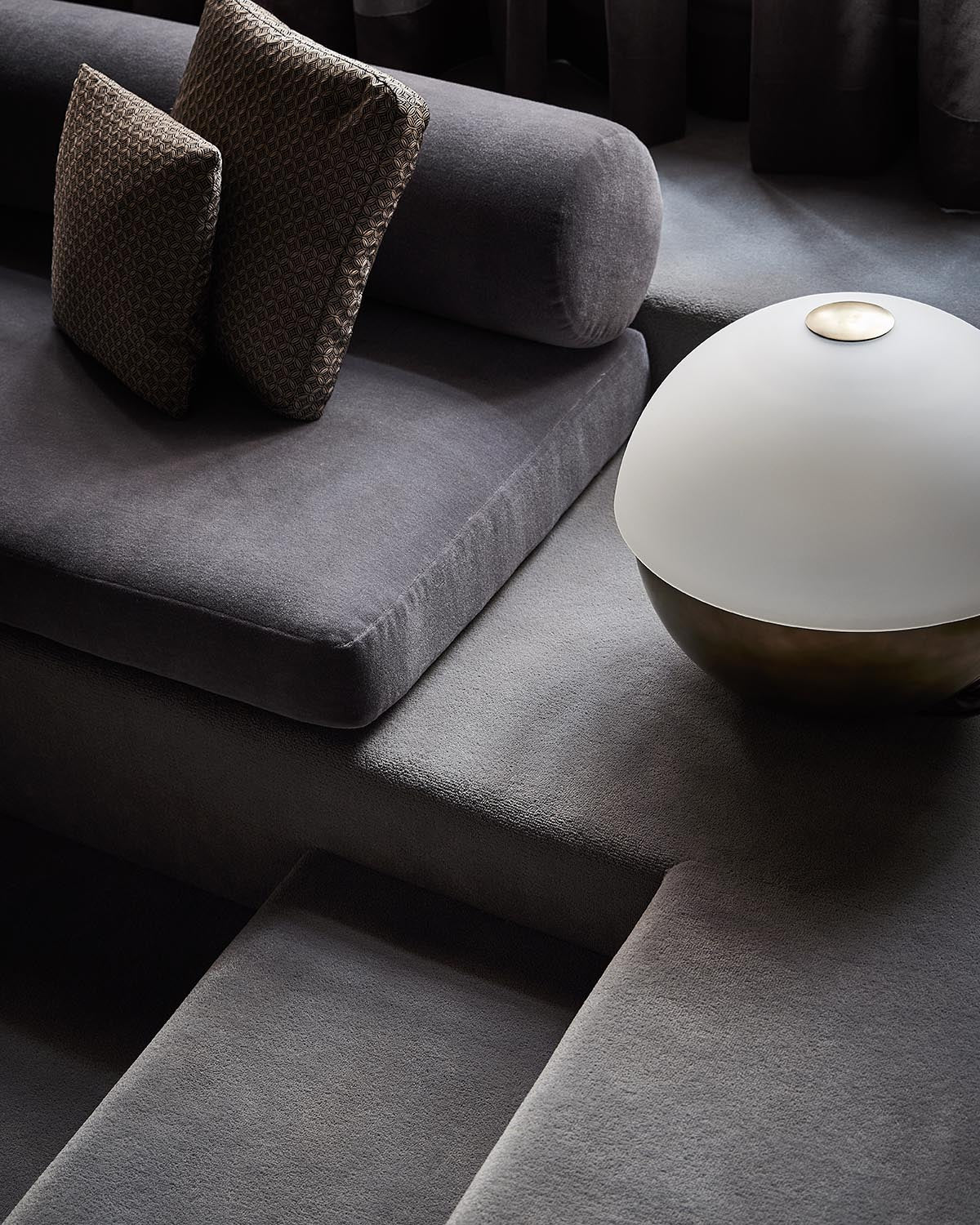 Close-up of a modern dark gray fabric sofa with textured cushions and a round white and bronze table lamp on a matching surface