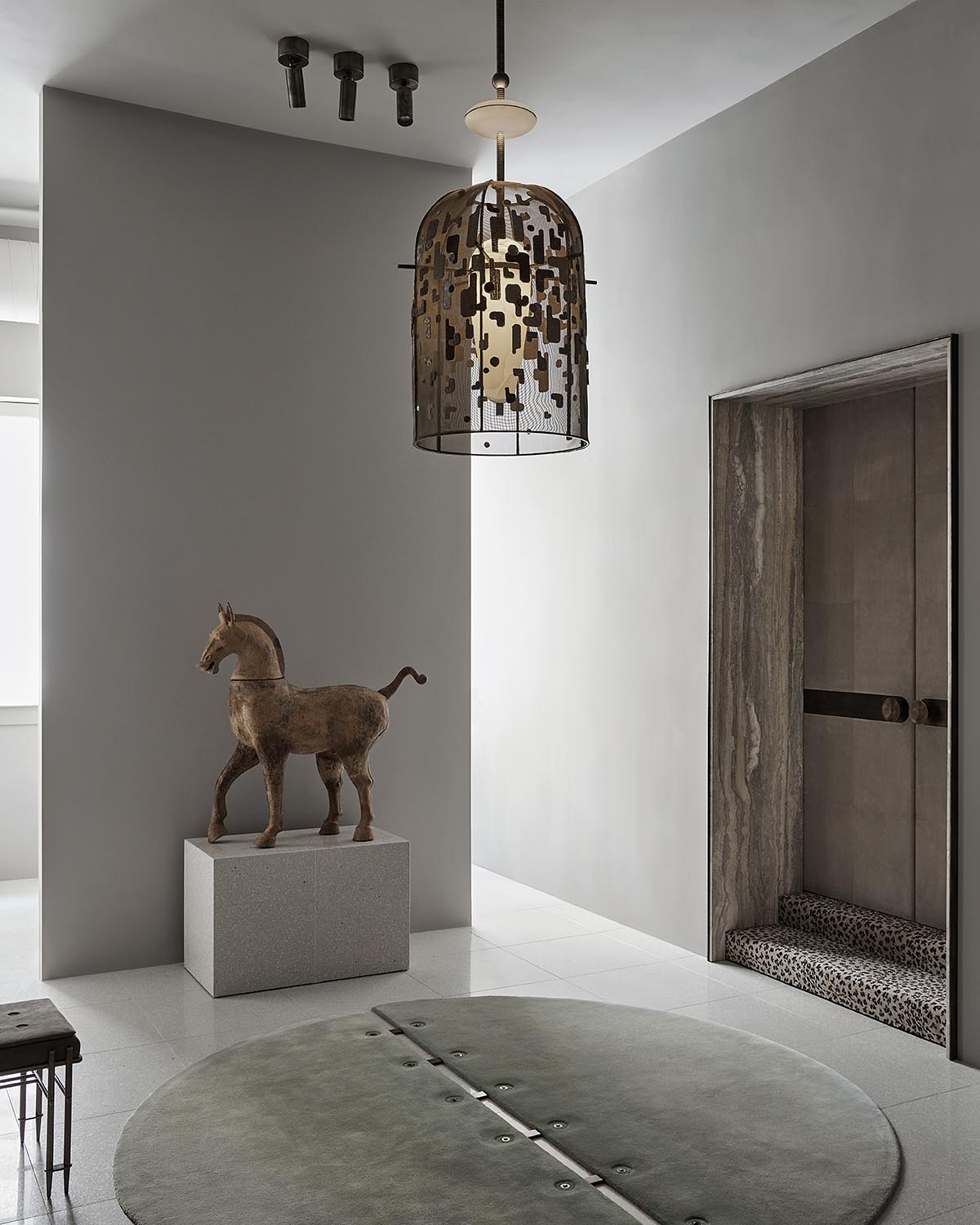 Minimalist interior with a sculptural horse figure on a pedestal, geometric pendant light, and neutral tones throughout the room