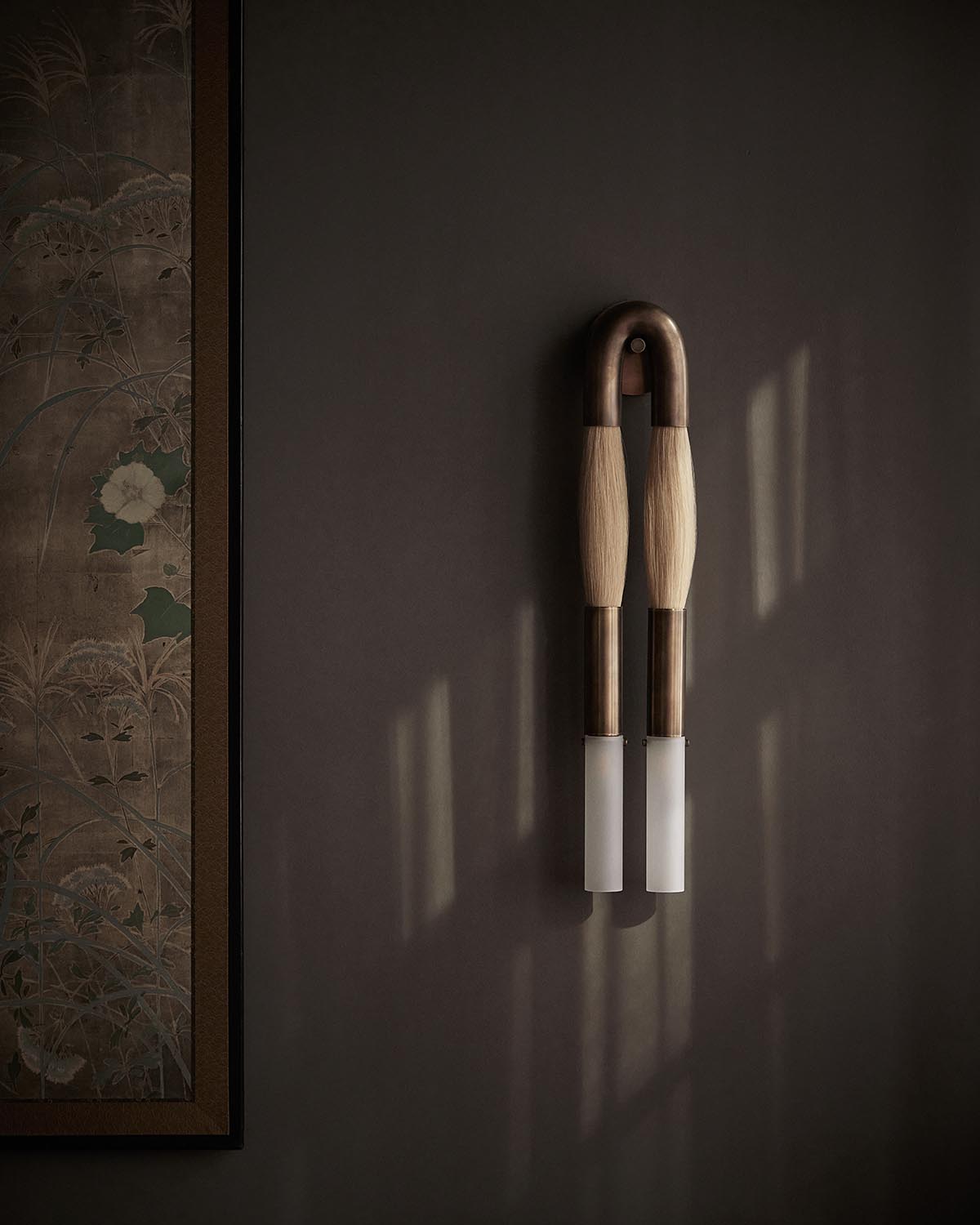 Pair of modern wall sconces with wooden handles and frosted glass shades on a muted dark gray wall beside framed botanical artwork