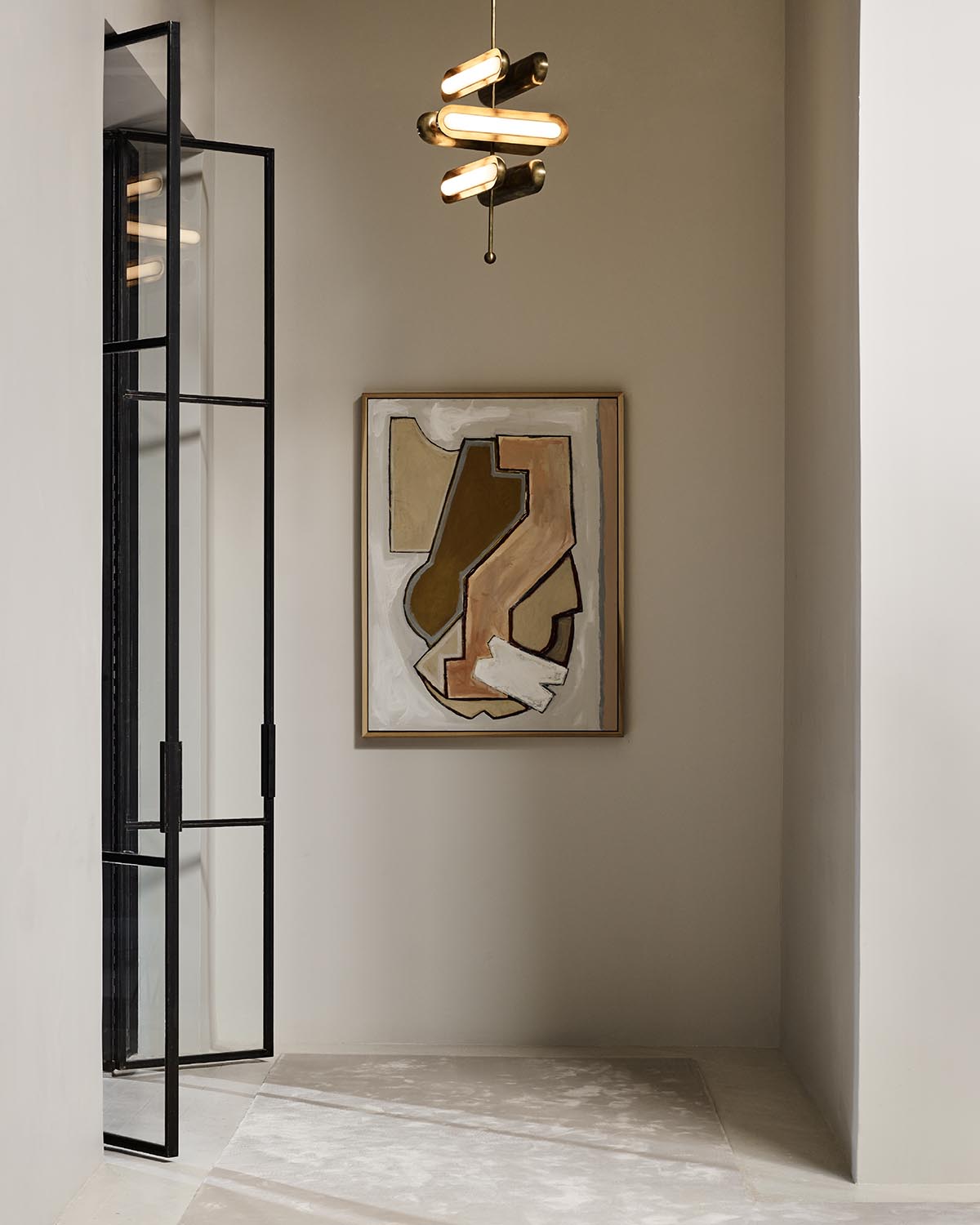 Minimalist corner with abstract geometric painting in muted tones, black metal-framed glass door, and modern ceiling light fixture
