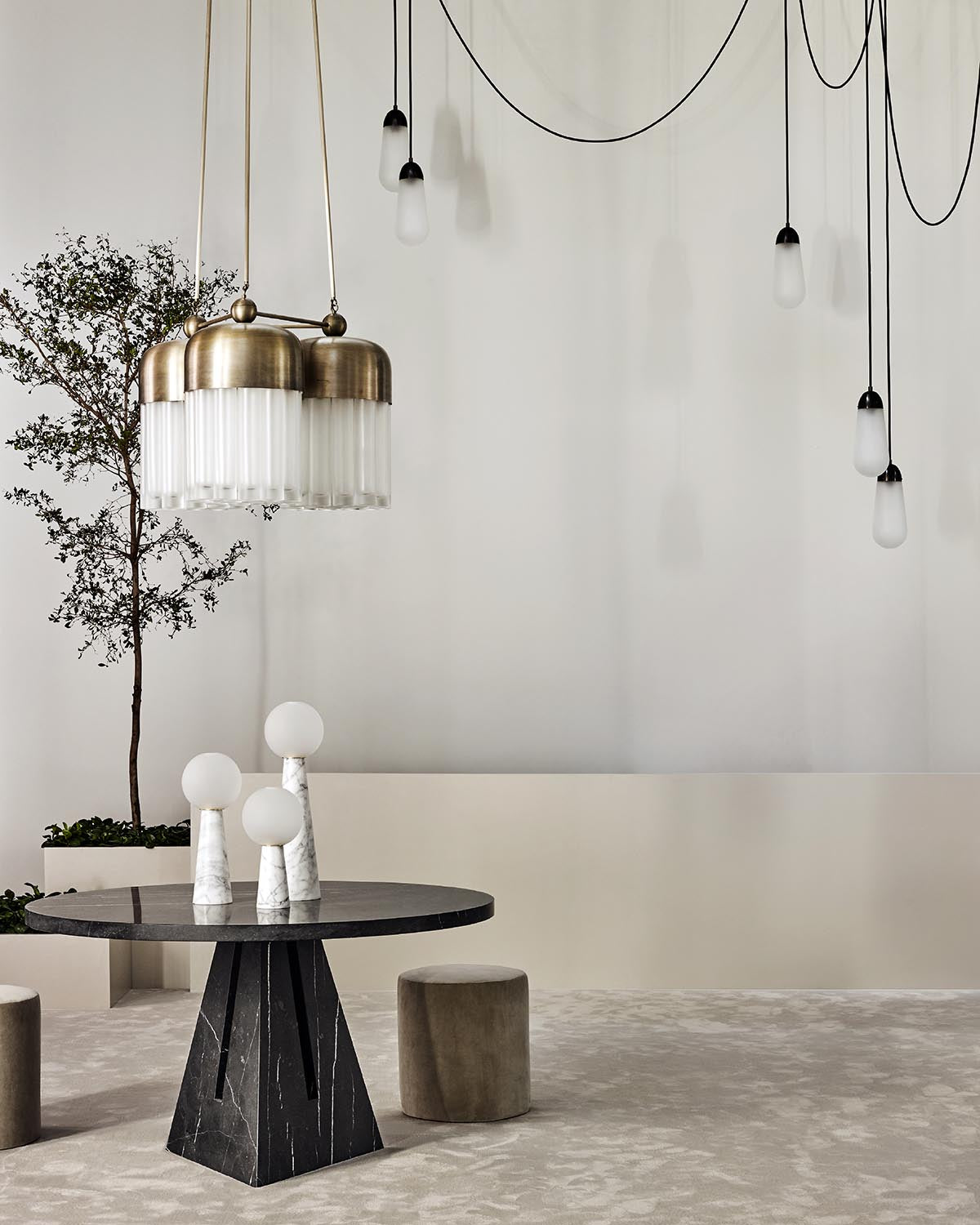 Minimalist interior with black marble round table, three white globe lamps, hanging pendant lights, and a potted tree on beige carpet
