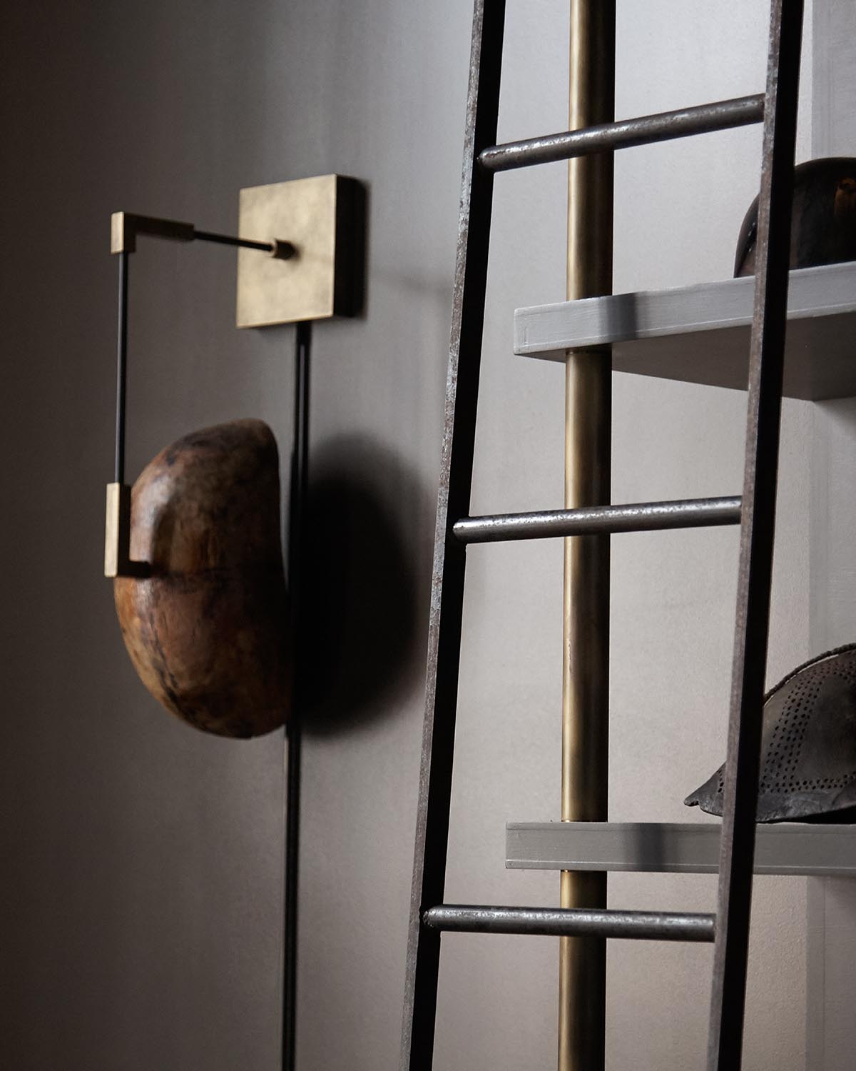 Close-up of a rustic wooden wall sculpture mounted beside a black metal ladder with brass accents against a muted wall