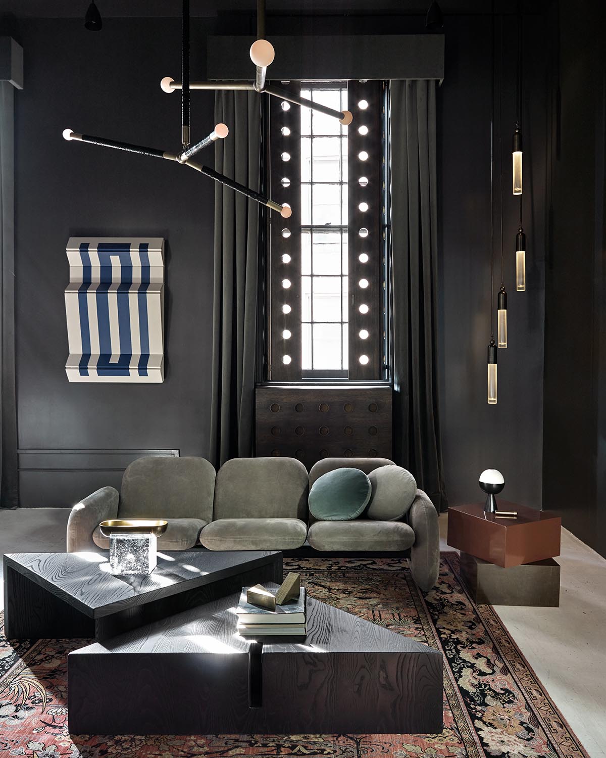 Contemporary dark living room with curved velvet sofa, geometric black coffee tables, sculptural wall art, and pendant lights.
