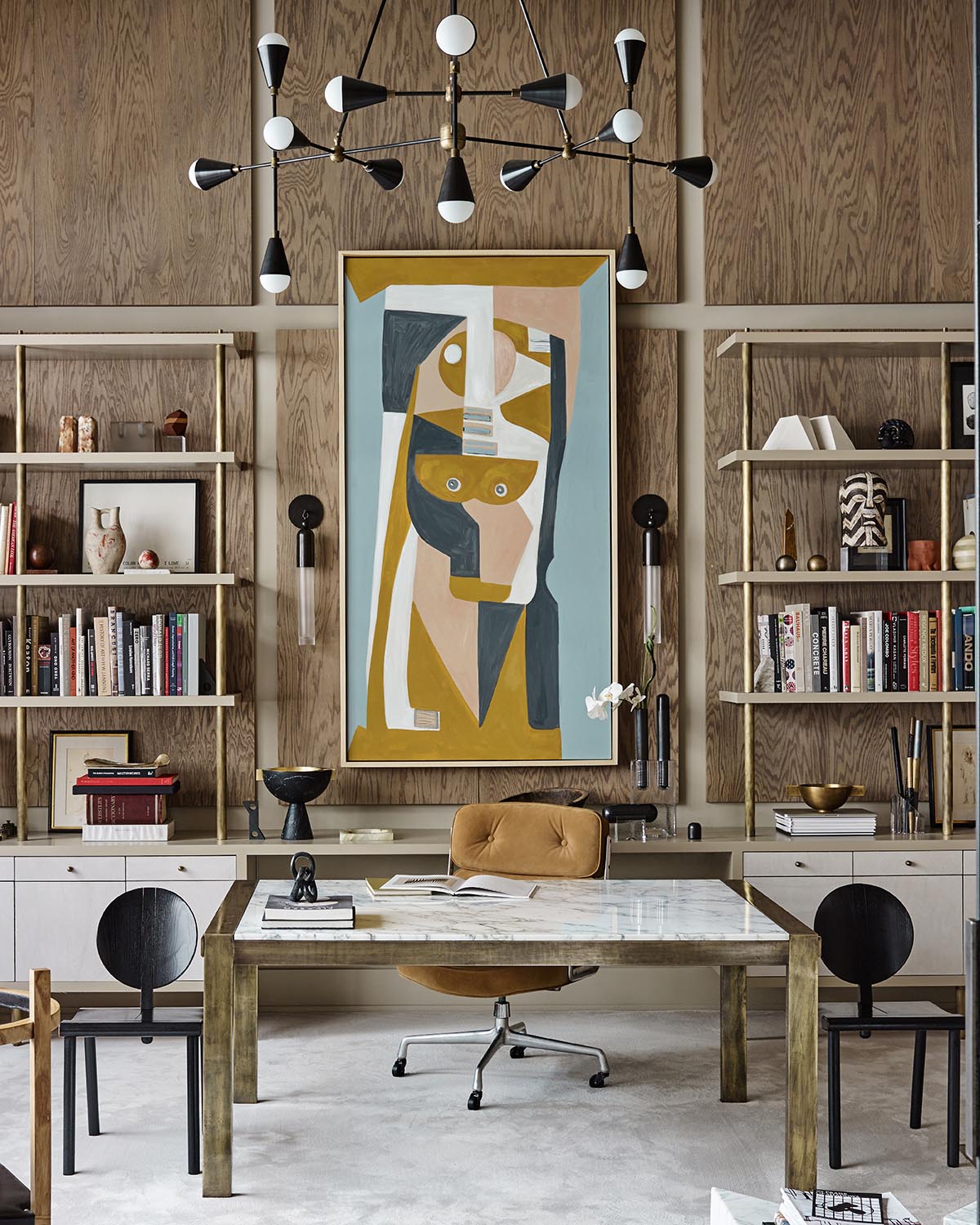 Modern office space with abstract artwork, wooden shelving filled with books and decor, and a marble top desk with seating