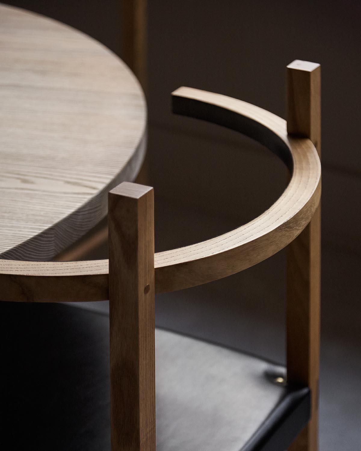 Close-up of a wooden chair with curved backrest and vertical supports next to a round wooden table top.