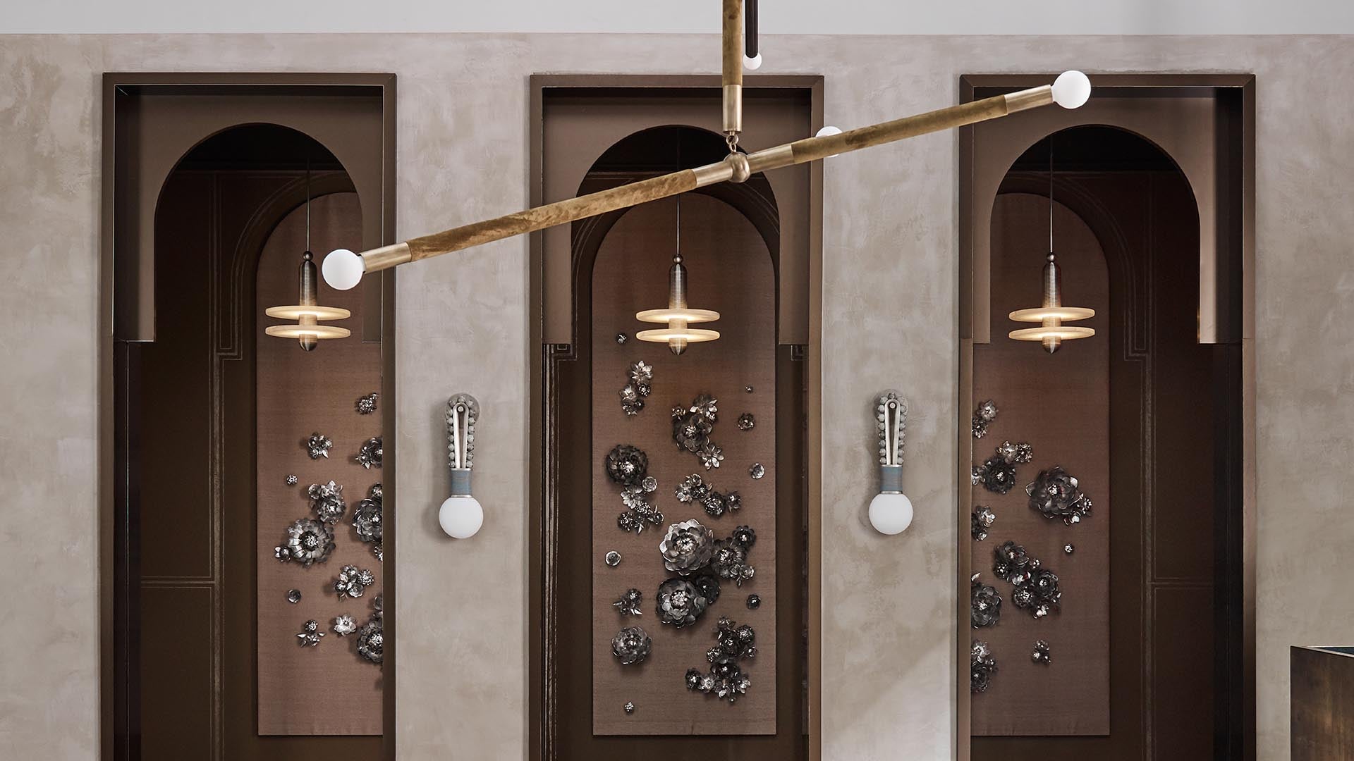 Three arched wall niches with abstract metallic floral sculptures and modern pendant lights in a neutral-toned interior