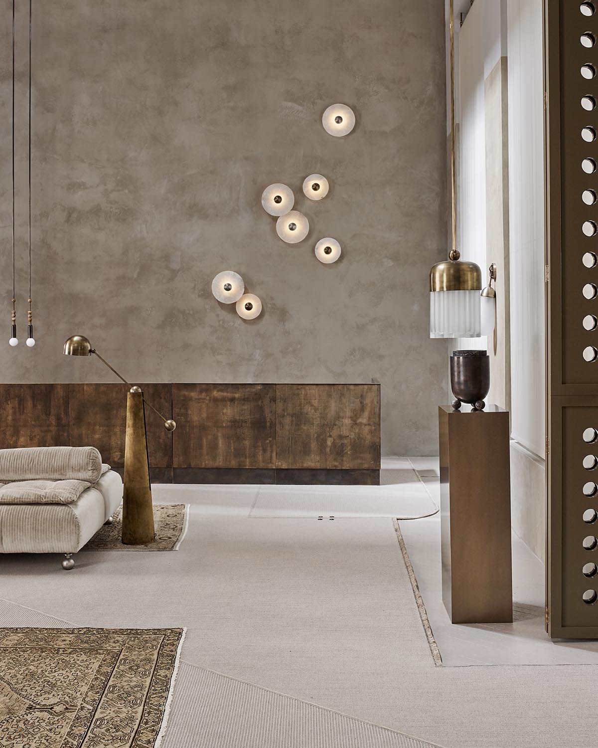 Minimalist room with textured concrete wall, cluster of circular wall lights, low brown cabinet, and neutral-toned furniture
