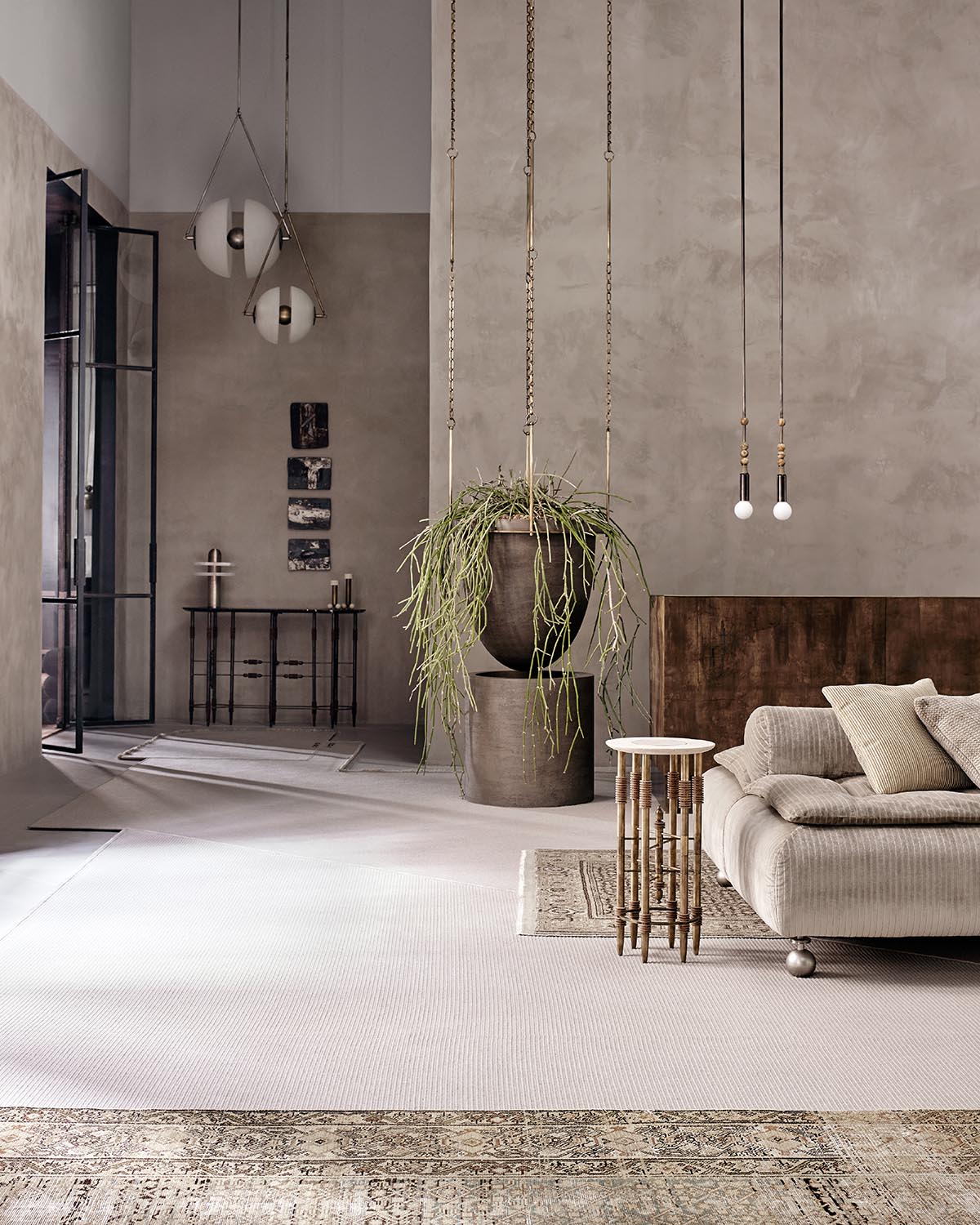 Minimalist living space with beige corduroy sofa, tall hanging plant in large pot, wooden side table, and pendant lights against textured wall