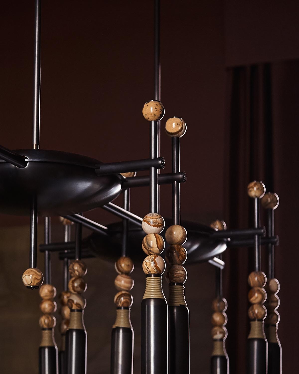 Close-up of modern chandelier featuring black metal rods and decorative light brown wooden beads against a dark background