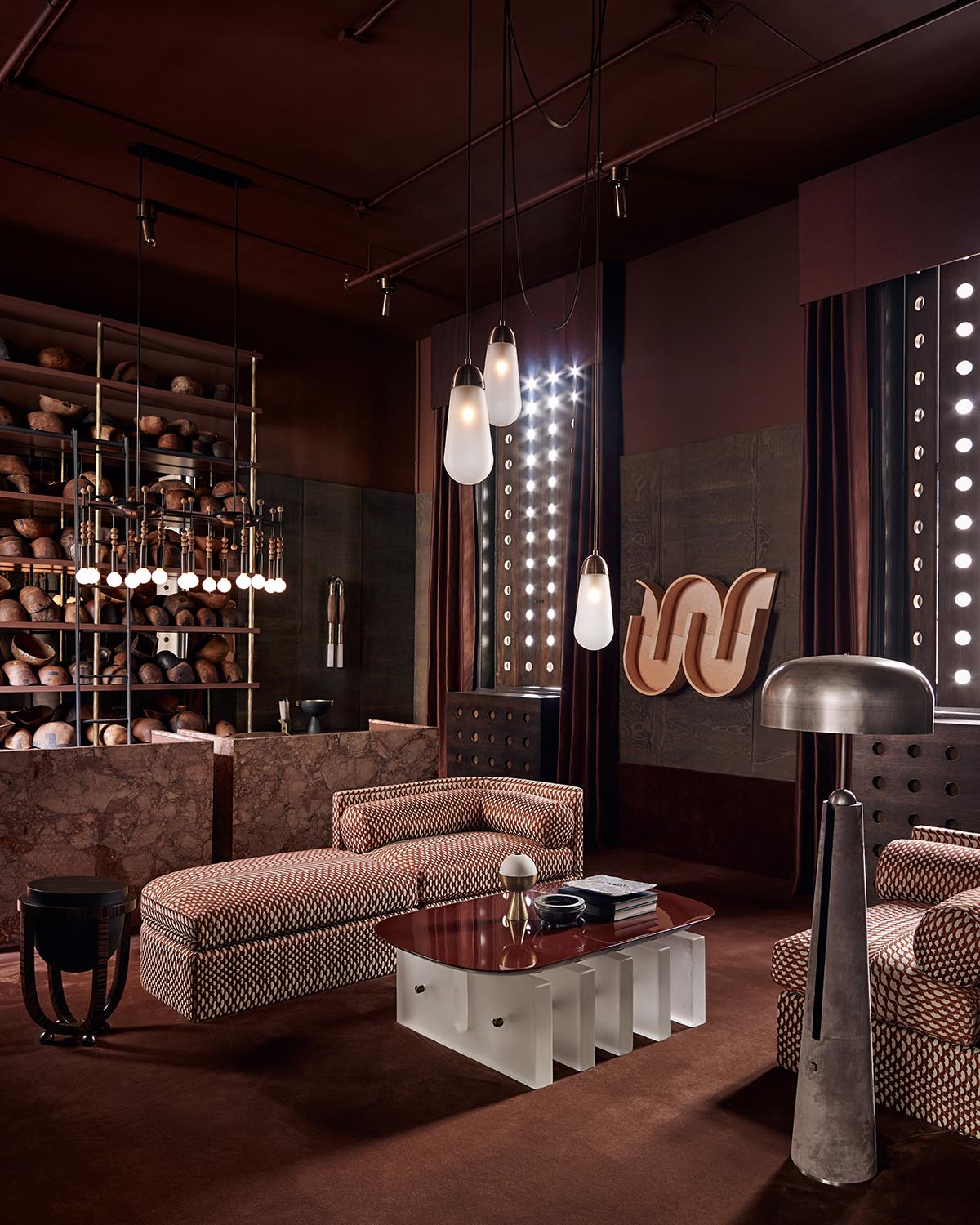 Living room with patterned sectional sofa, sculptural coffee table, floor lamp, and shelves filled with round pottery pieces