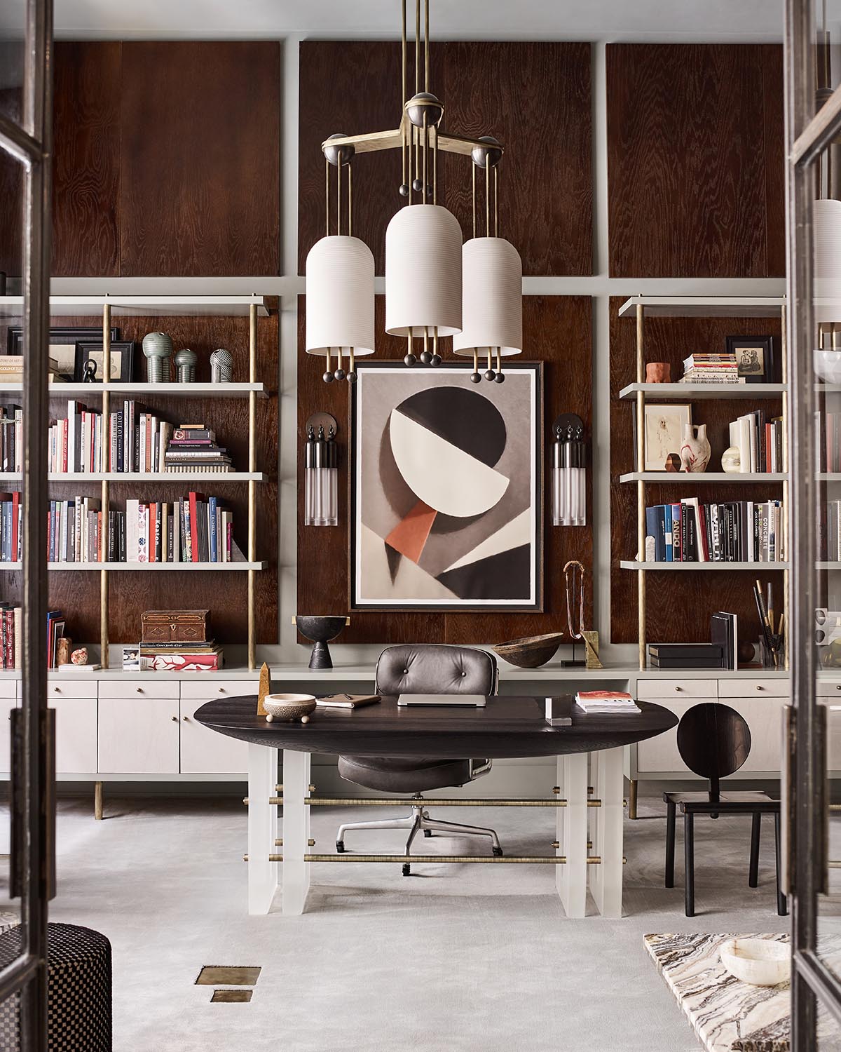 Modern office space with dark wood paneling, white shelving, abstract artwork, and a large black and white desk with chairs