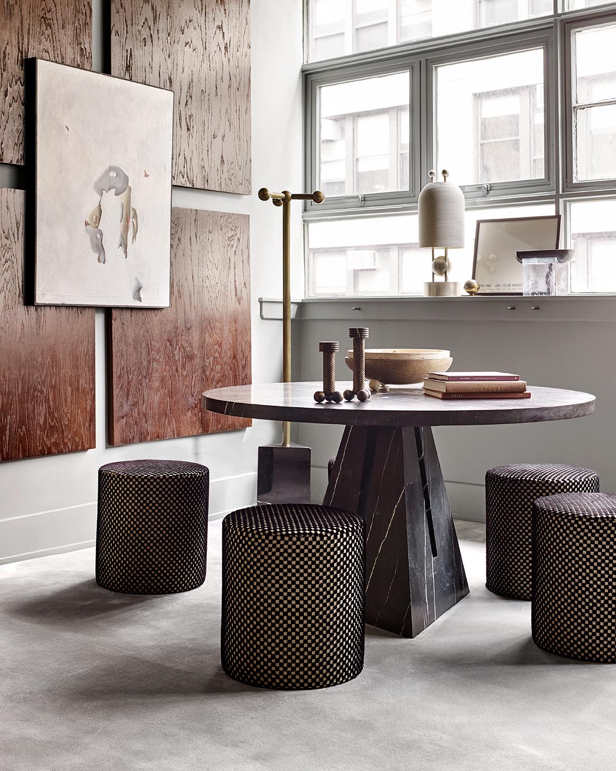 Minimalist dining area with round dark marble table, four patterned stools, textured wooden wall panels, and large windows.
