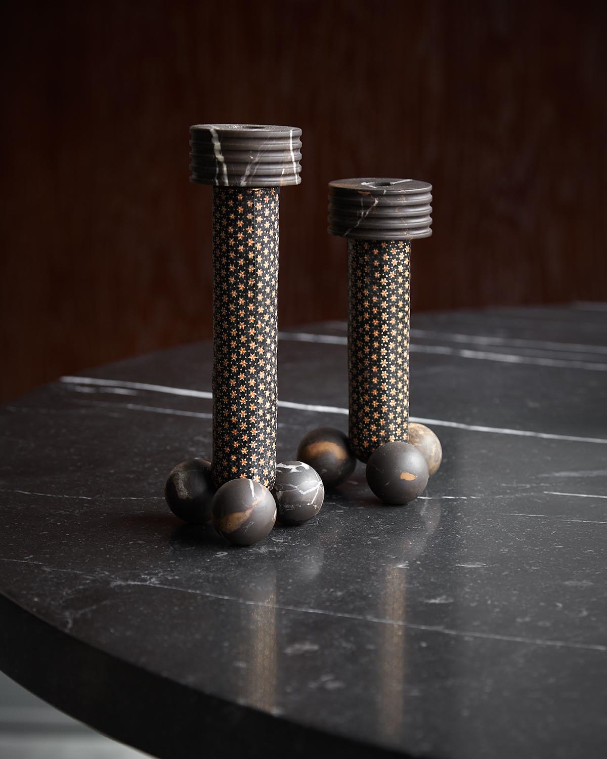 Two cylindrical decorative objects with star-patterned surfaces and spherical bases on a dark marble table top
