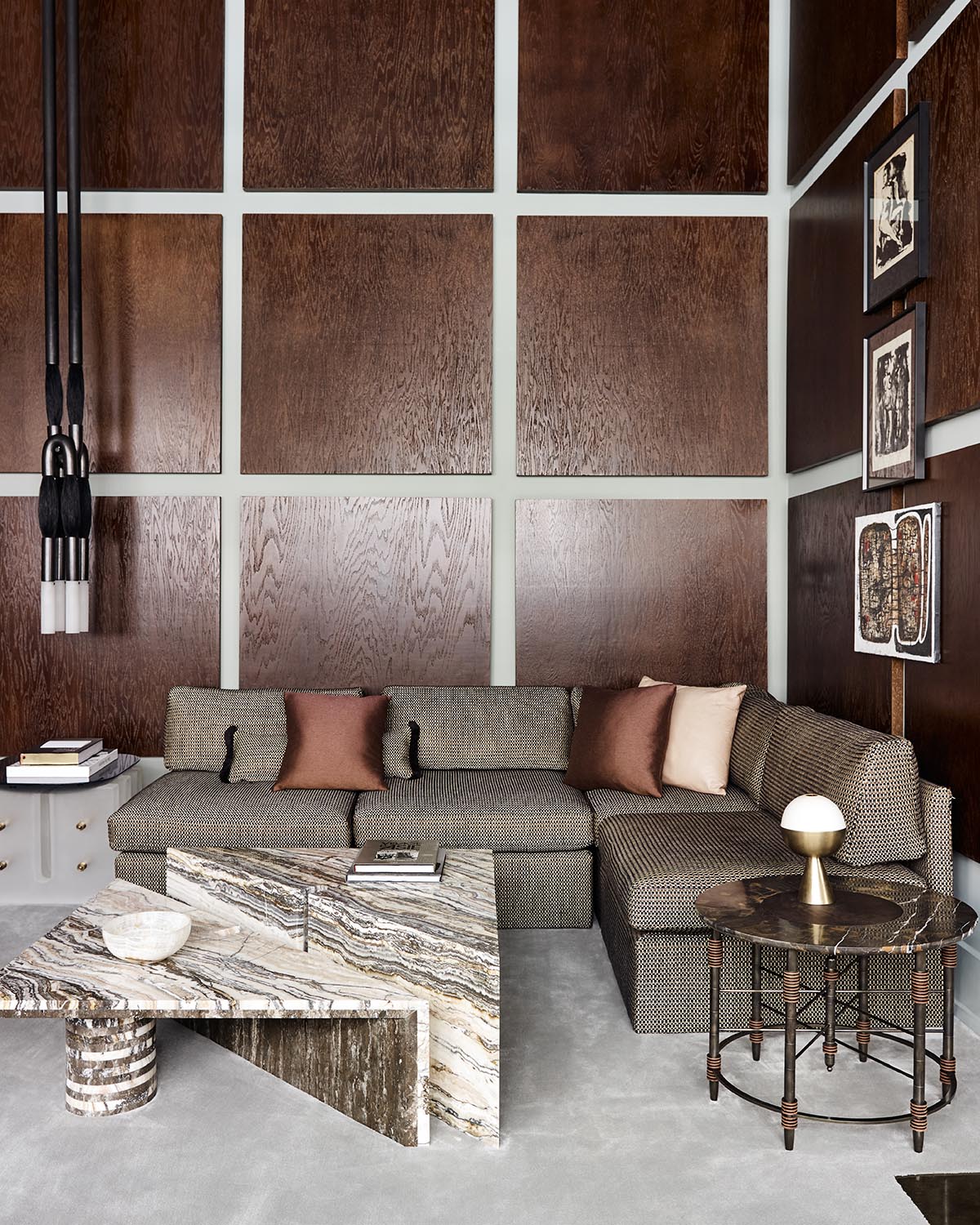 Corner living room with textured brown panel walls, gray sectional sofa, marble coffee table, and round side table with lamp