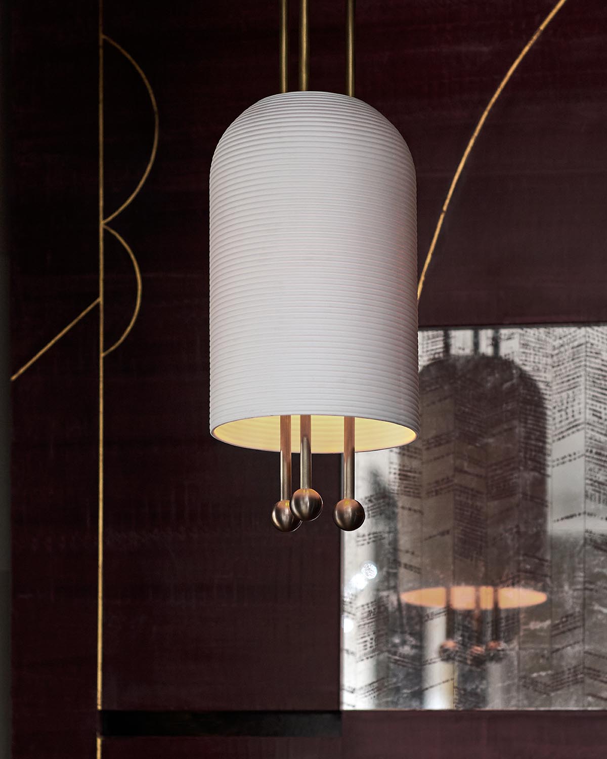 Close-up of a white cylindrical pendant light with three metal rods and spherical ends, reflected on decorative dark wall panel