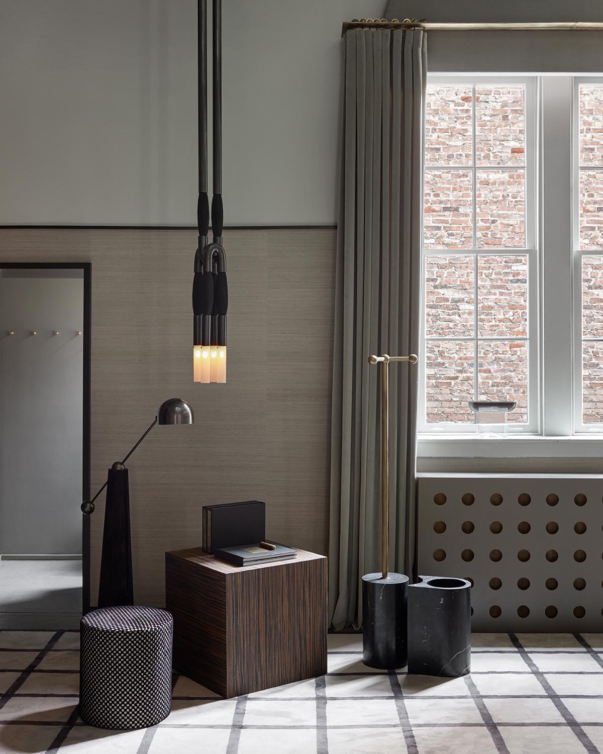 Minimalist corner with a striped wooden cube table, patterned ottoman, tall black lamp, and window with heavy curtains