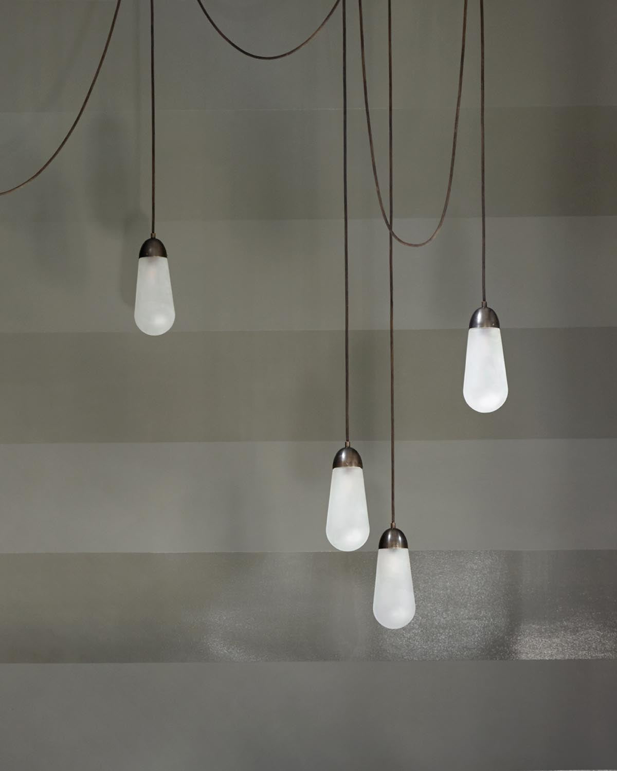 Four frosted glass pendant lights with dark metal fittings hanging at varying heights against a muted striped wall