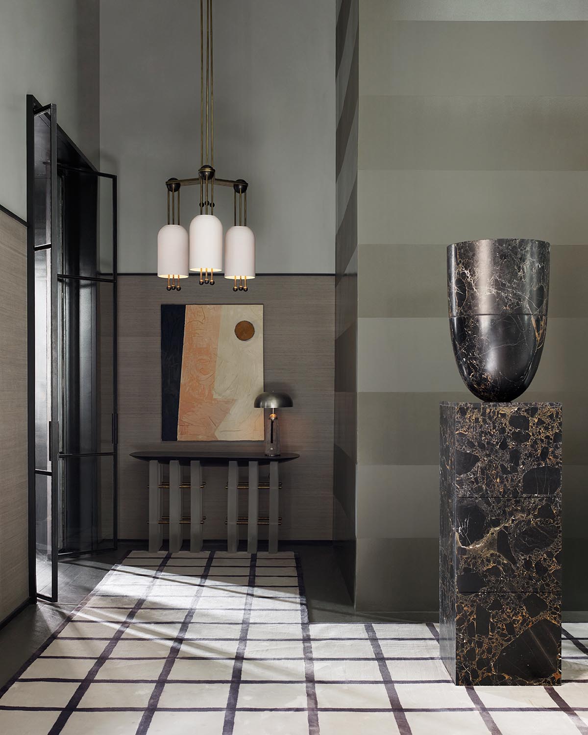 Minimalist hallway with striped rug, dark marble sculpture on pedestal, wall art, and pendant lights above console table