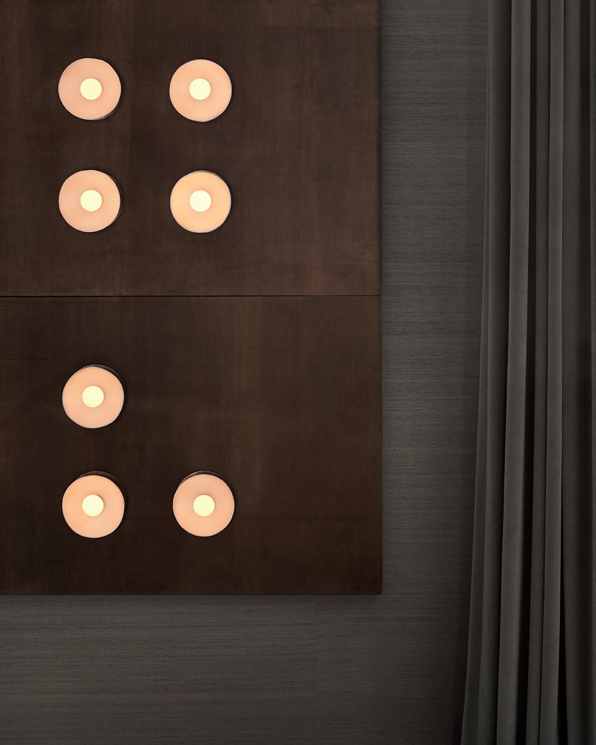 Top-down view of two dark rectangular panels with six round illuminated lights arranged in domino patterns against a textured gray wall next to gray curtains