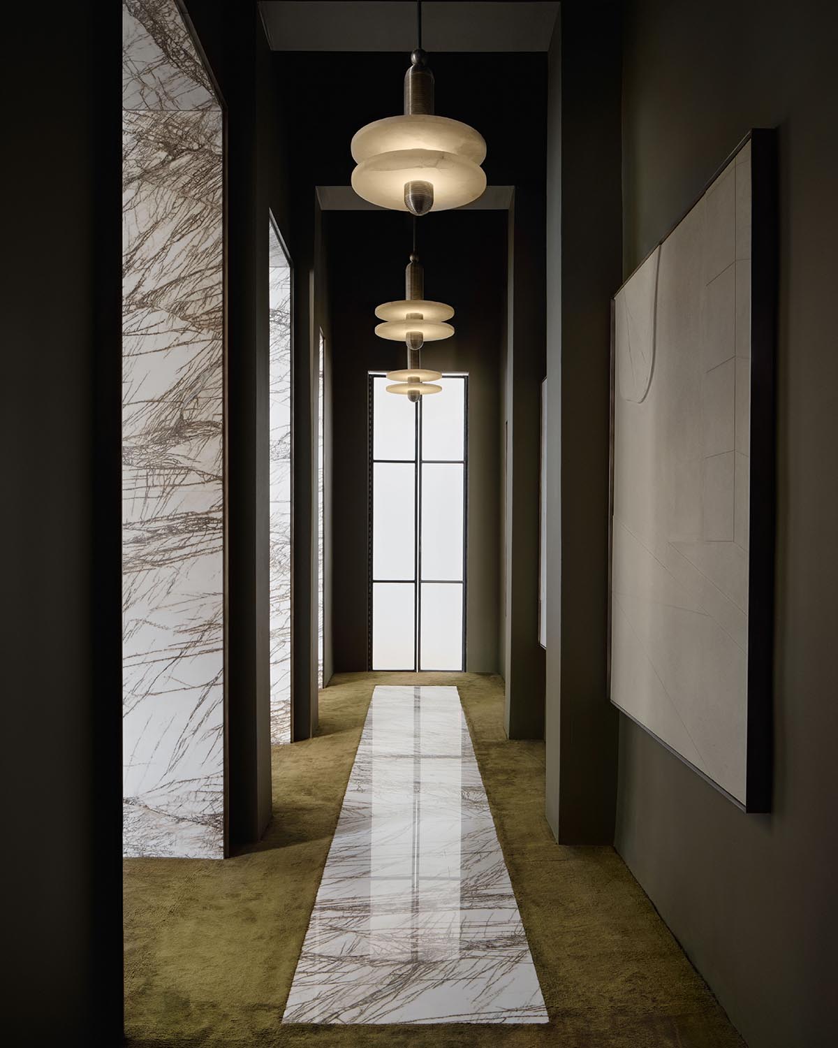 Narrow hallway with olive green carpet, white marble runner, three pendant lights, and abstract wall art on dark walls