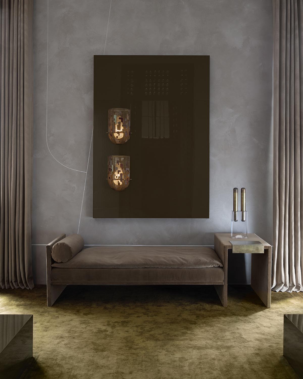 Minimalist sitting area with a dark padded bench, beige curtains, abstract wall art, and a small side table with decorative objects