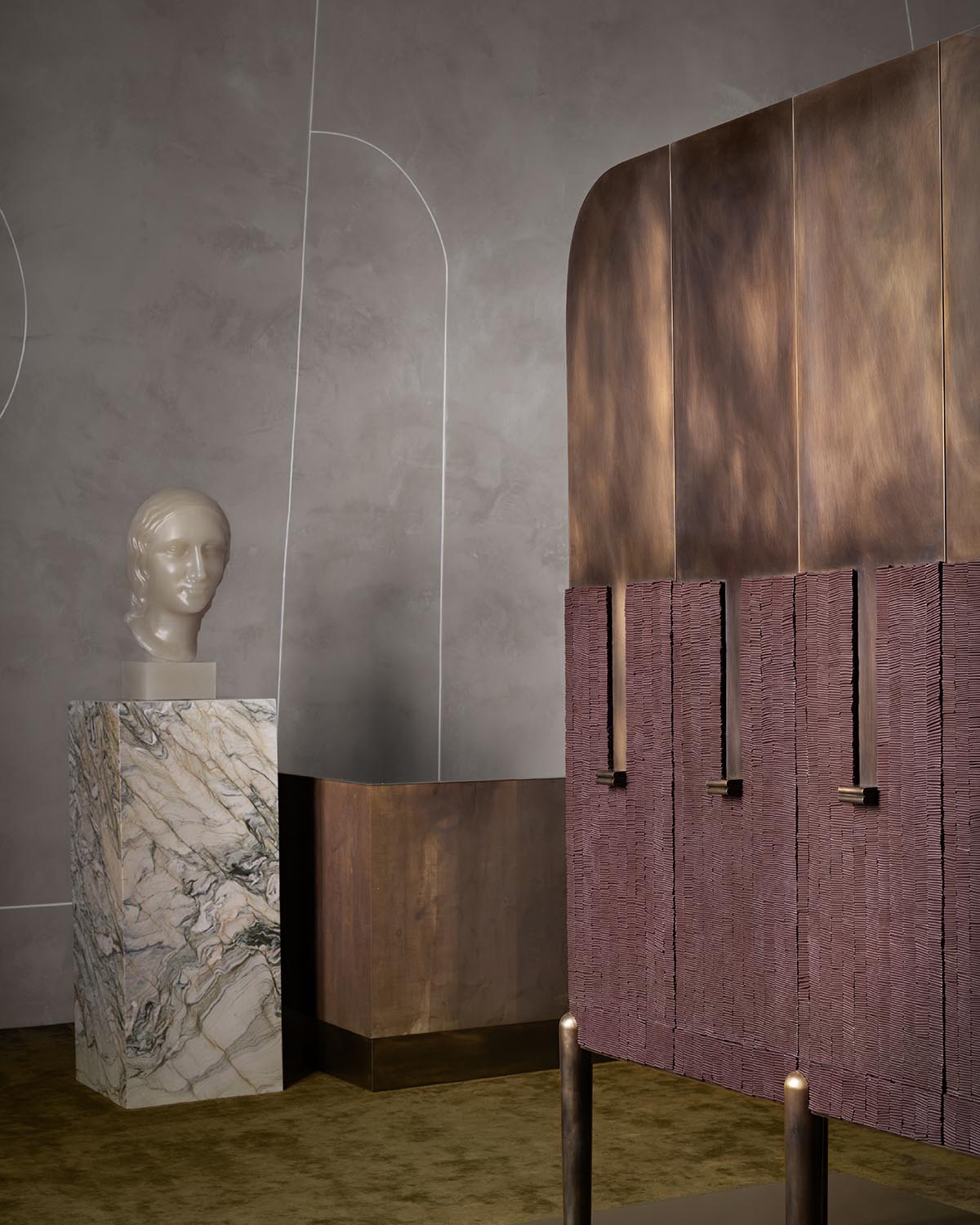 Interior corner with a marble pedestal holding a sculpted head and a textured bronze and mauve cabinet against a gray wall