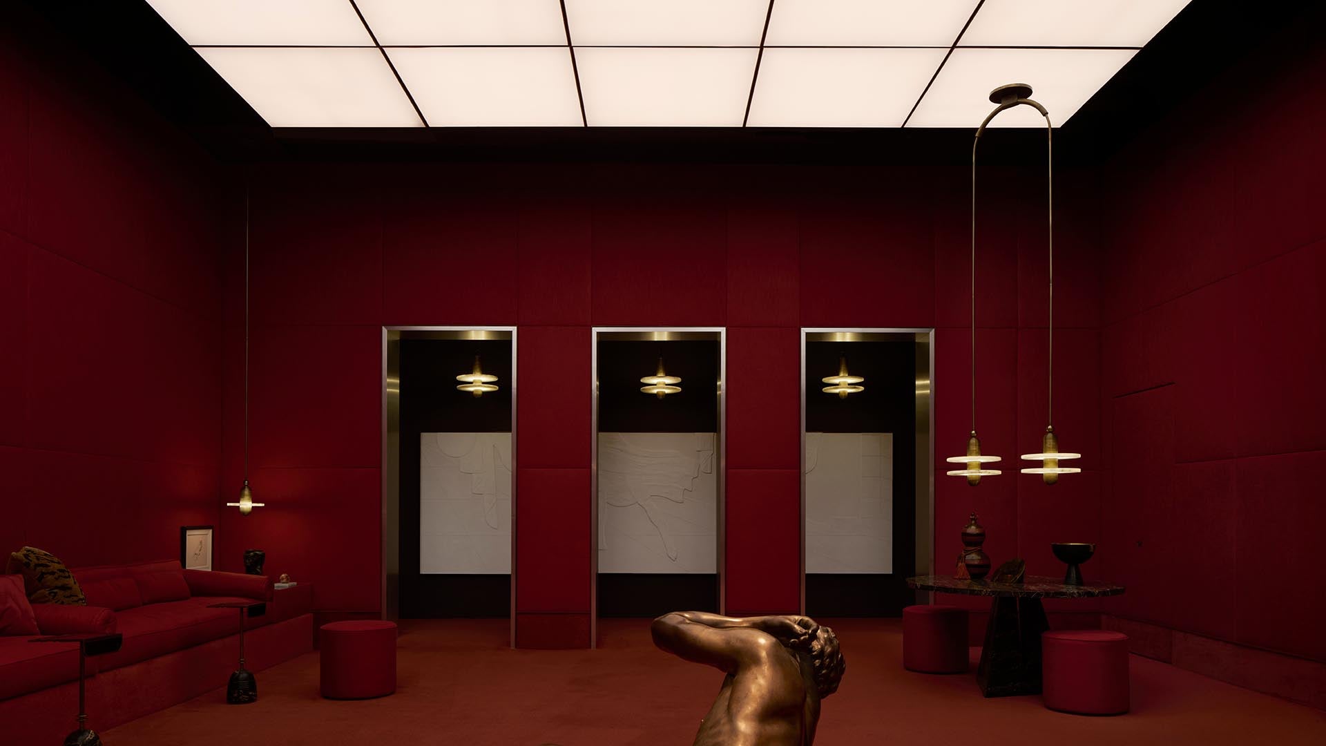 Minimalist room with deep red walls, three doorways, pendant lights, and a bronze statue in the center under a lit ceiling panel