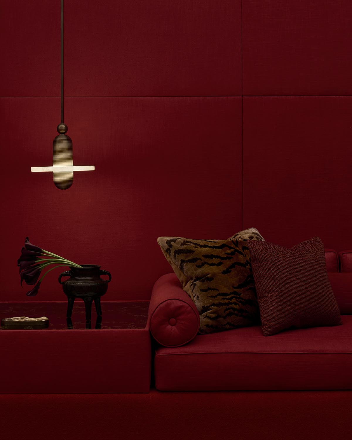 Dark red minimalist living room corner with velvet sofa, animal print and textured pillows, black vase, and pendant light