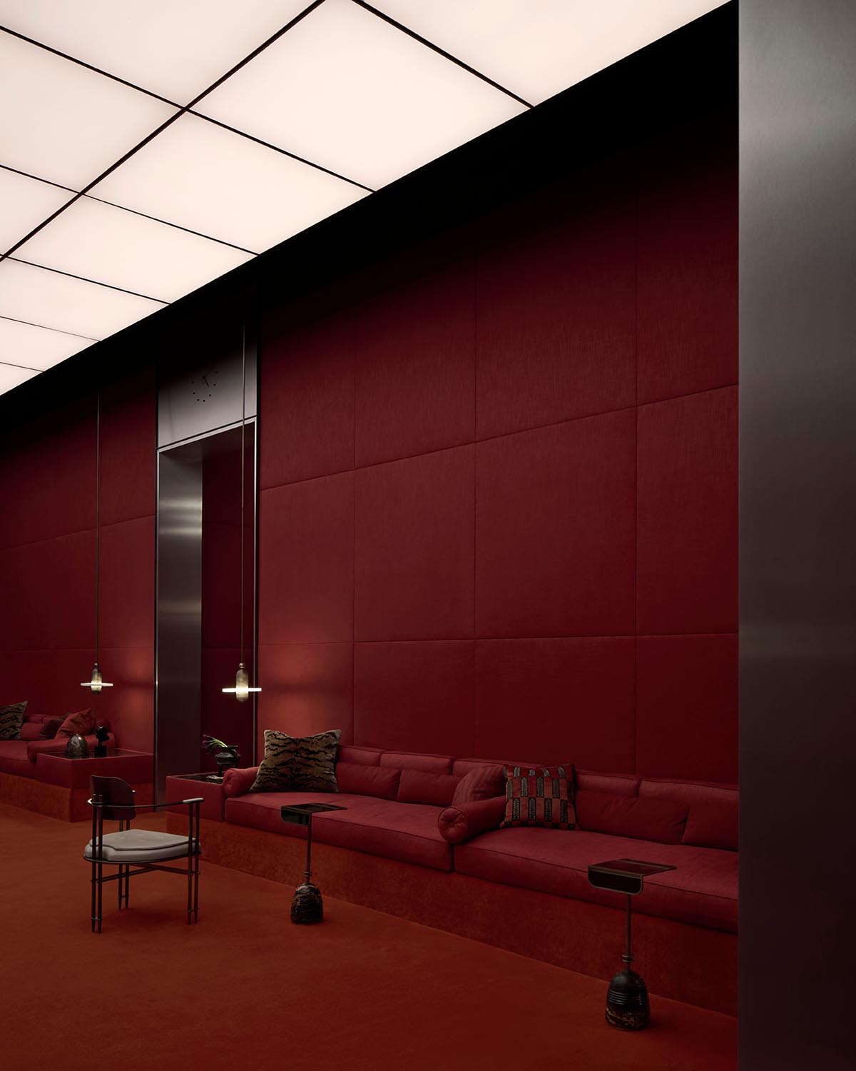 Modern lounge area with deep red upholstered walls and sofa, black framed chair, small side tables, and overhead panel lighting