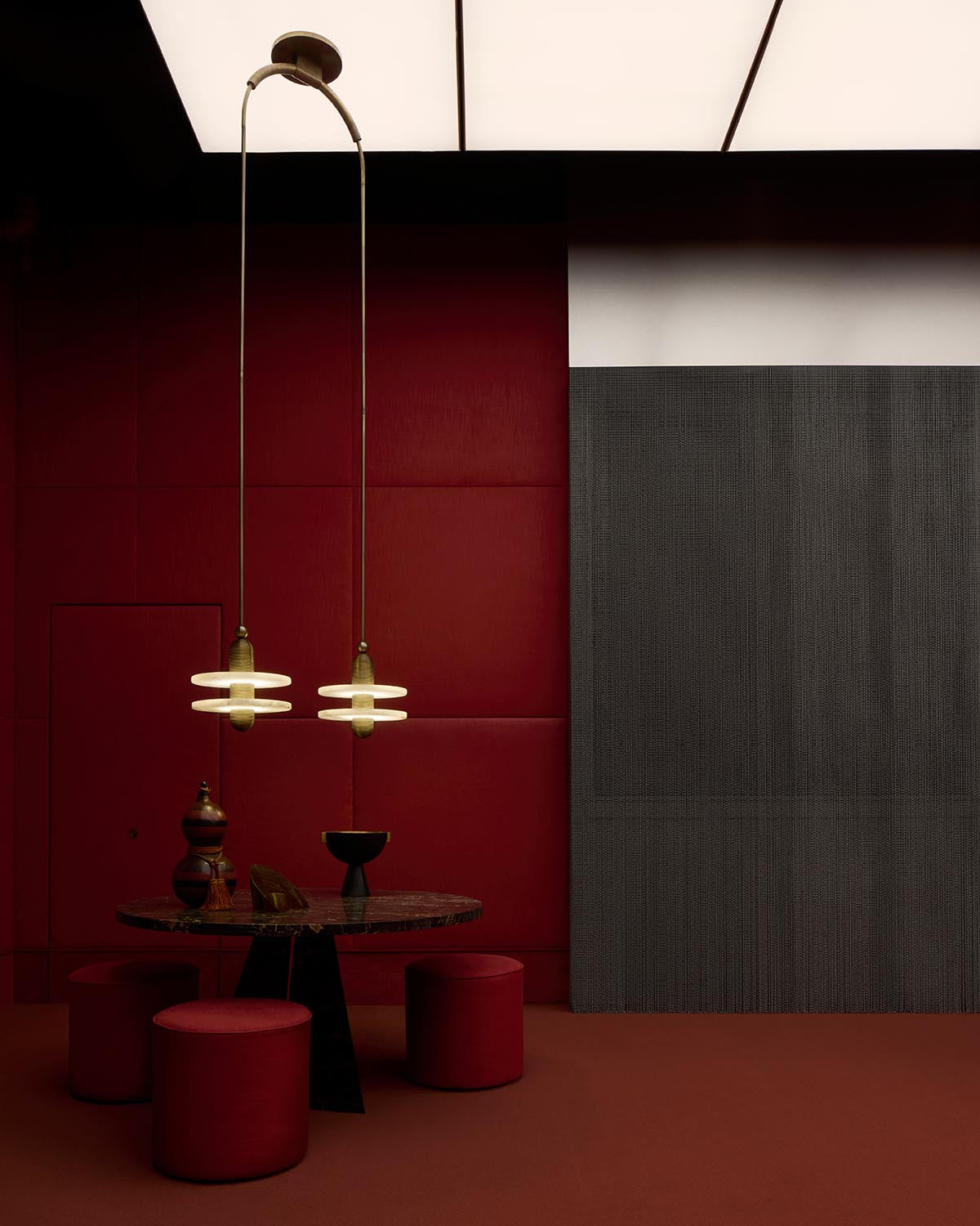 Minimalist dining space with round marble table, four red cylindrical stools, and two pendant lights against red and dark gray walls