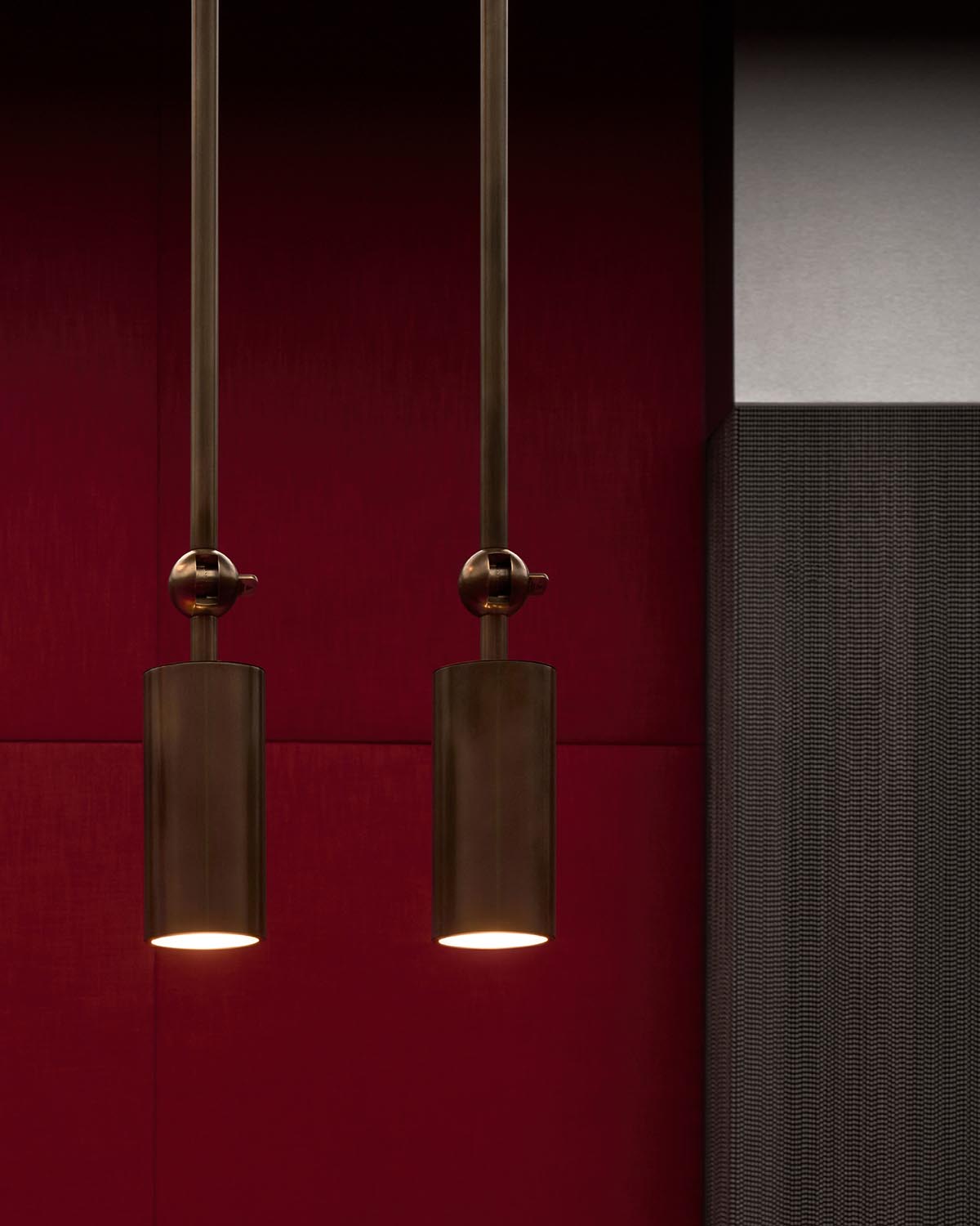 Two cylindrical bronze pendant lights hanging against a deep red and textured dark gray wall background