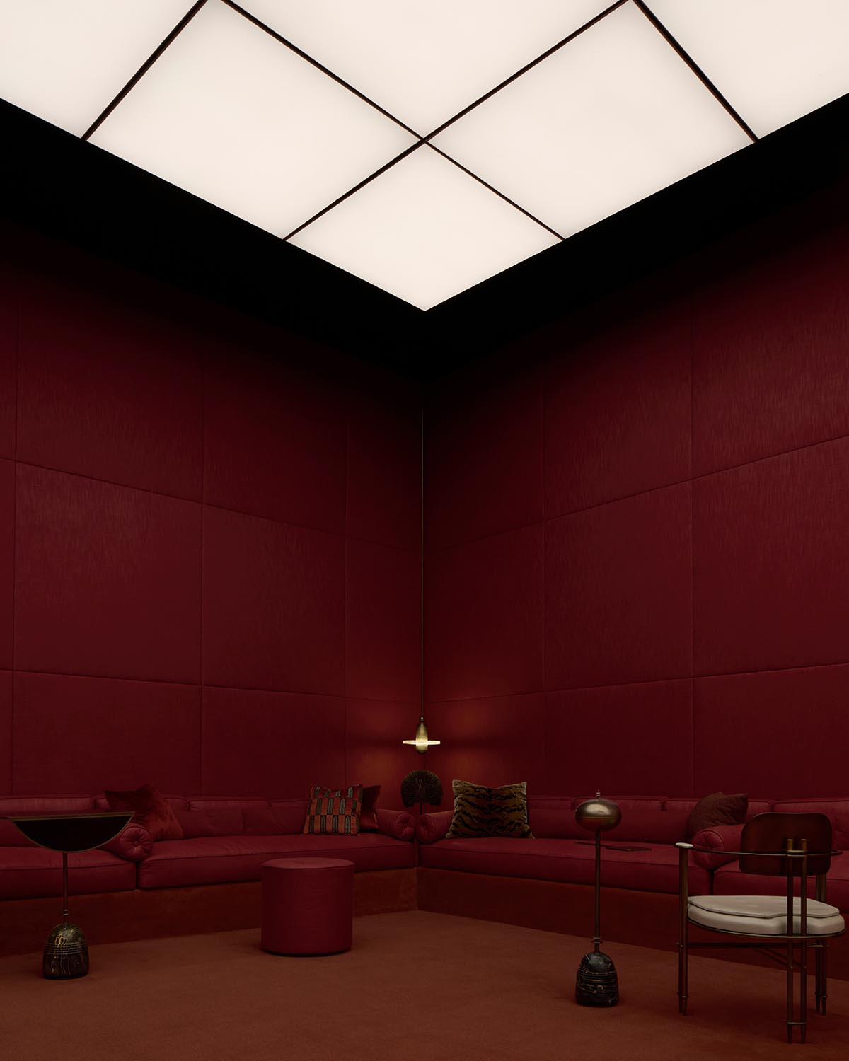 Minimalist corner seating area with deep red walls, cushioned bench, hanging pendant light, and modern sculptural accents