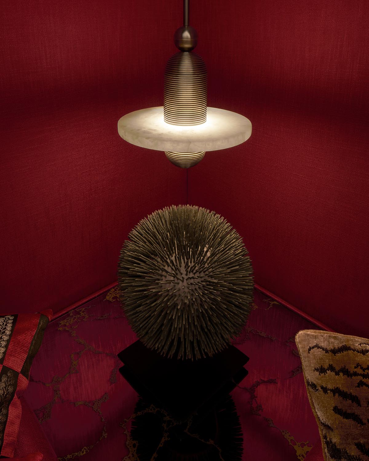 Dimly lit scene with a spiked spherical sculpture on a dark pedestal beneath a ribbed pendant light and deep red textured walls.