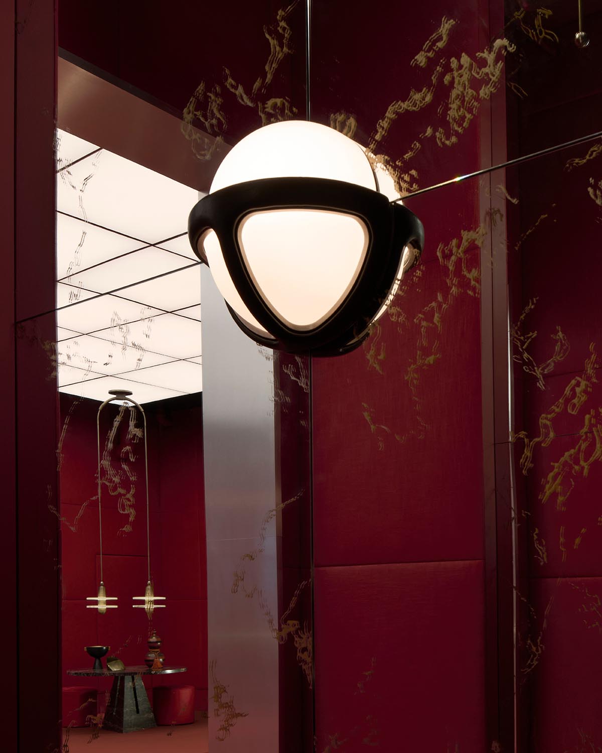 Close-up of a modern spherical pendant light with black geometric frame hanging in a room with red textured walls and mirrors