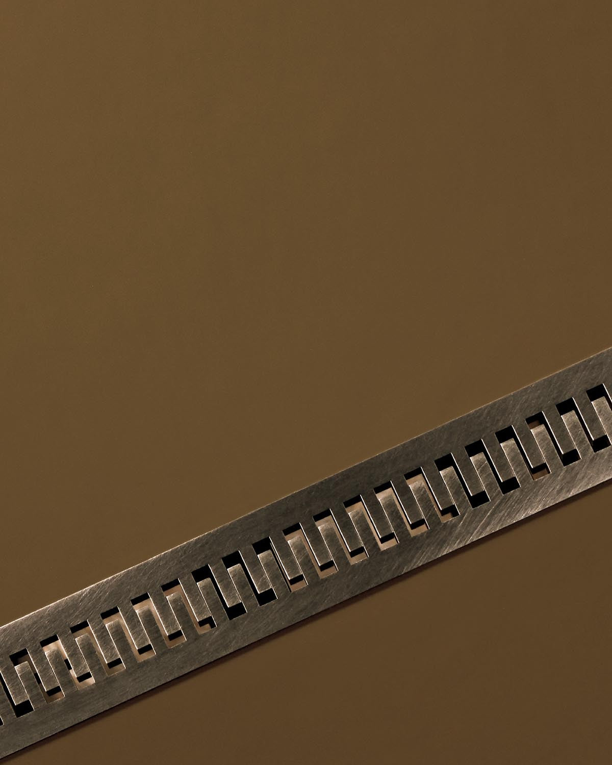 Brushed metal decorative strip with repeating rectangular cutouts on a smooth brown surface