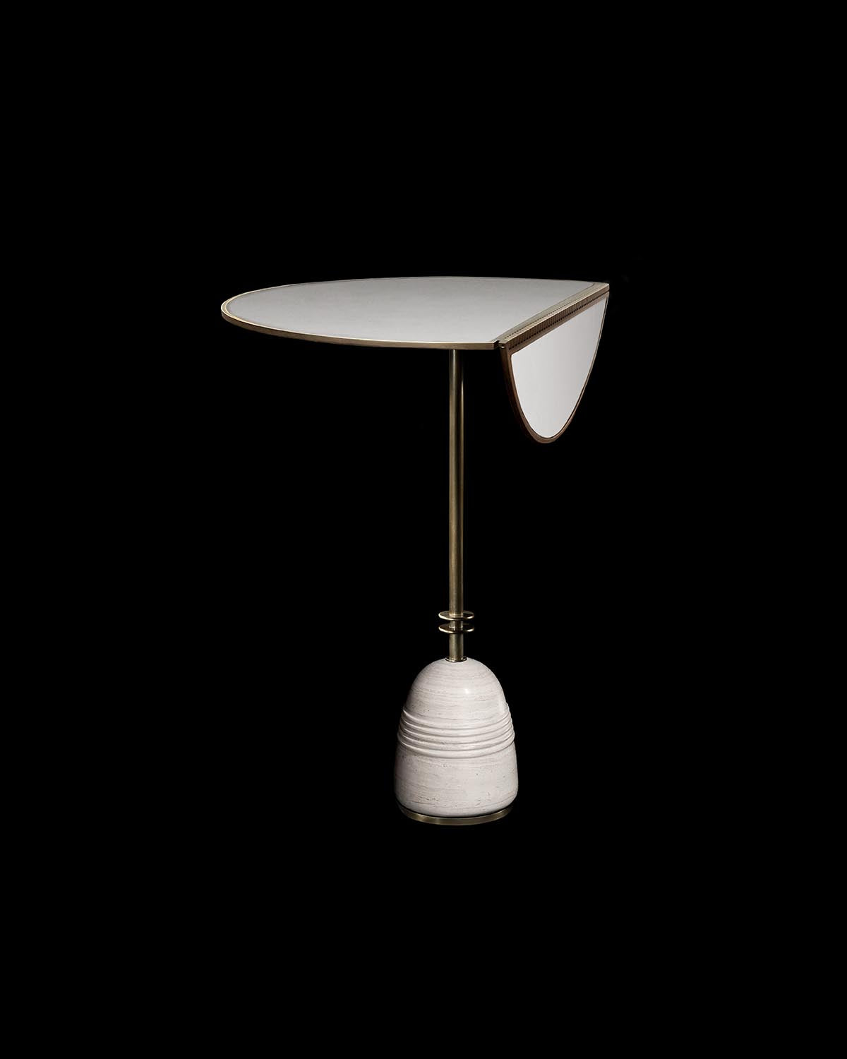 Minimalist bistro table with round white top and drop-leaf supported by brass rod and rounded stone base on black background