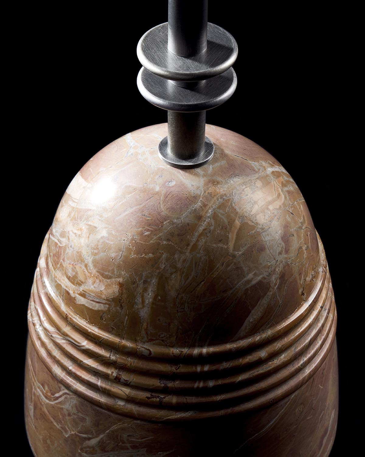 Close-up of rounded marble base with carved grooves and metal rod with circular discs against black background