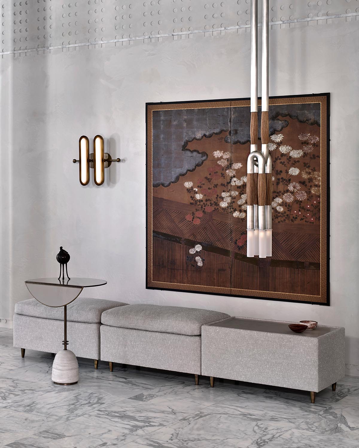 Minimalist bistro table with round glass top and metal base next to a long gray upholstered bench on marble floor