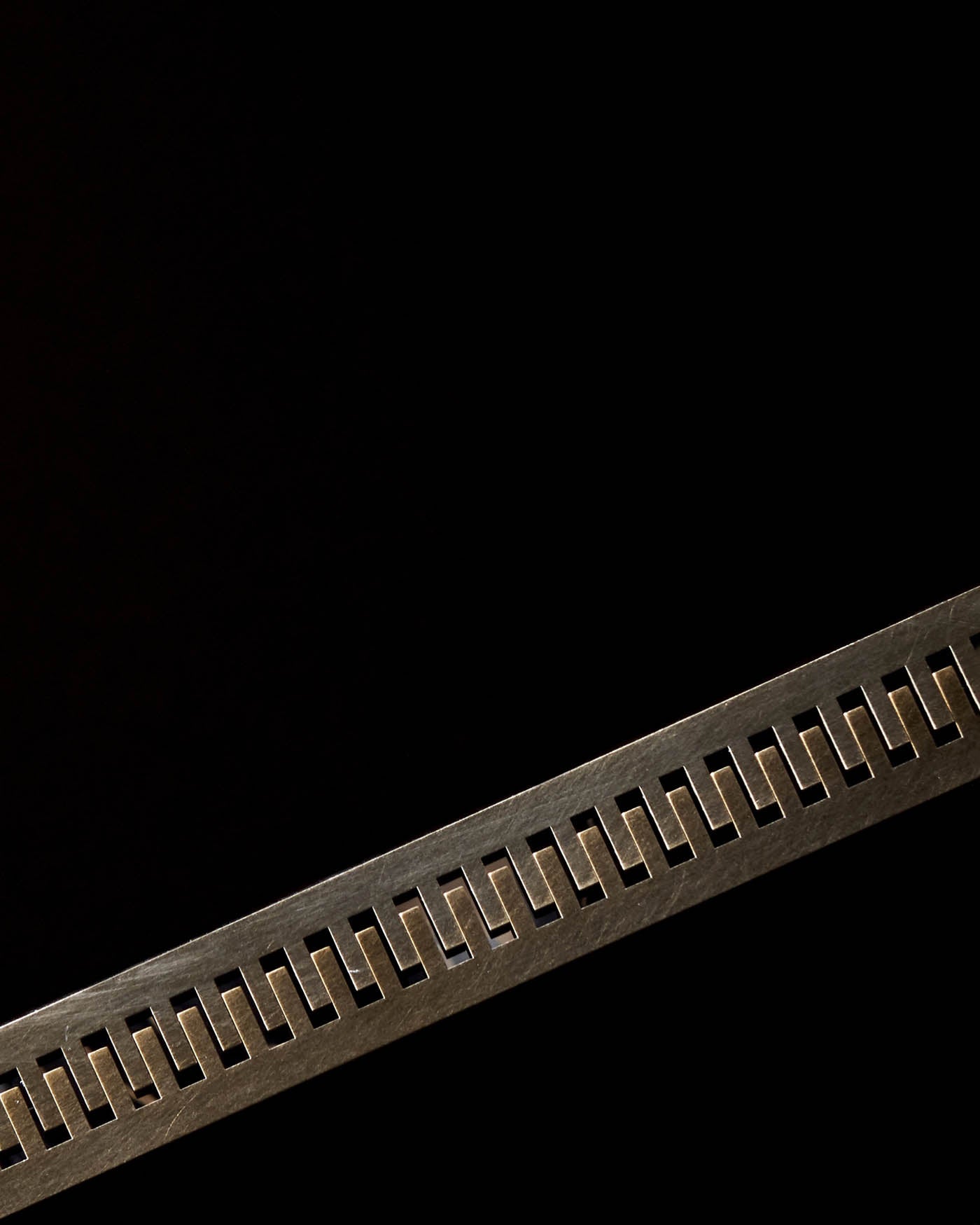 Close-up of a dark metal strip with evenly spaced rectangular cutouts against a black background