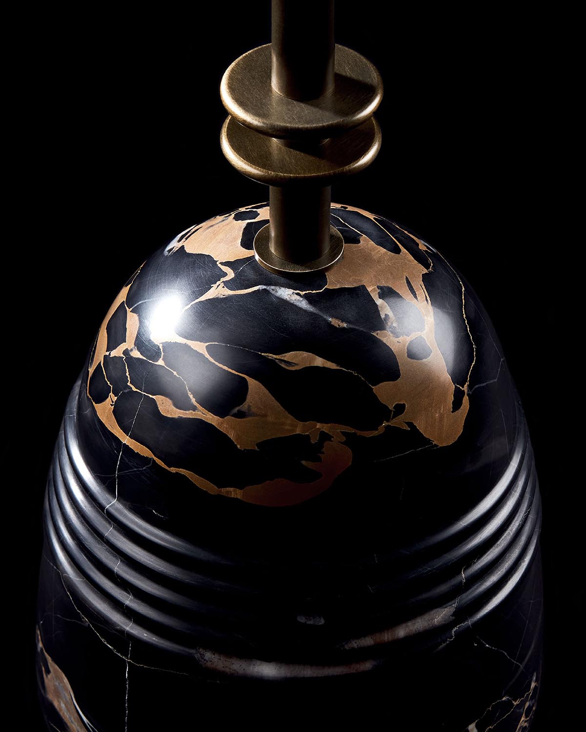 Close-up of black marble cocktail table base with gold veining and antique brass hardware against a black background